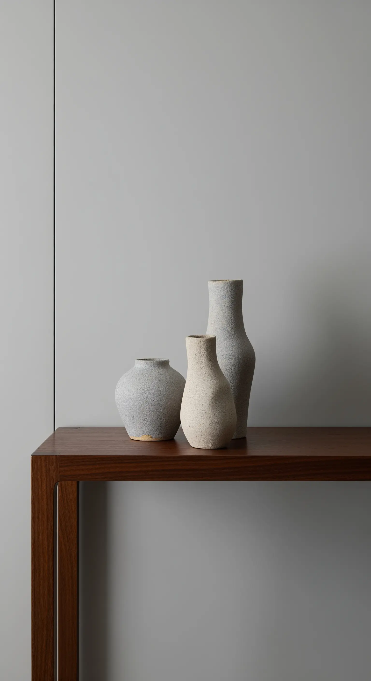 Drei Keramikvasen in Grau- und Beigetönen mit unterschiedlichen Texturen auf einem Holztisch.