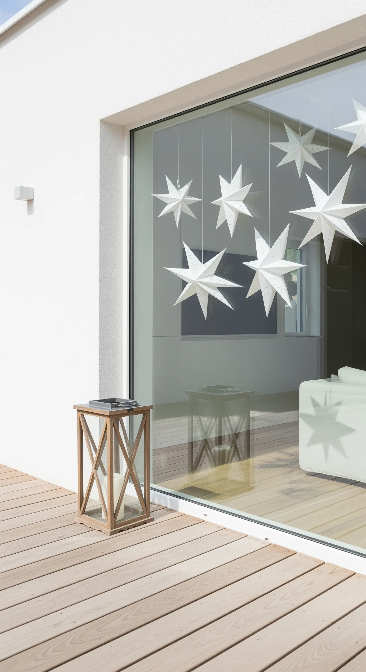 Große Fensterfront mit hängenden weißen Papiersternen und Holzlaterne draußen