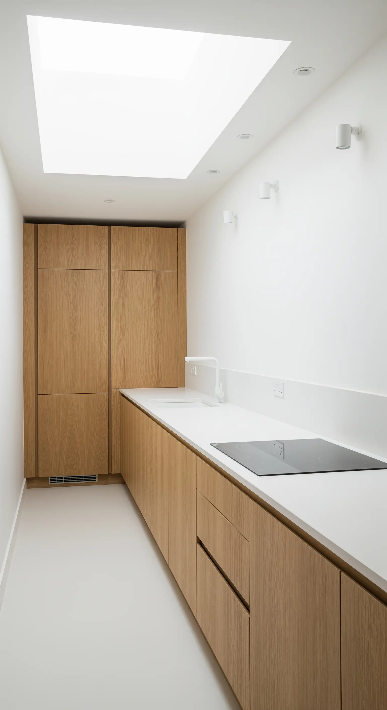 Schmale, minimalistische Küche mit Holzfronten und einem großen Oberlicht an der Decke.