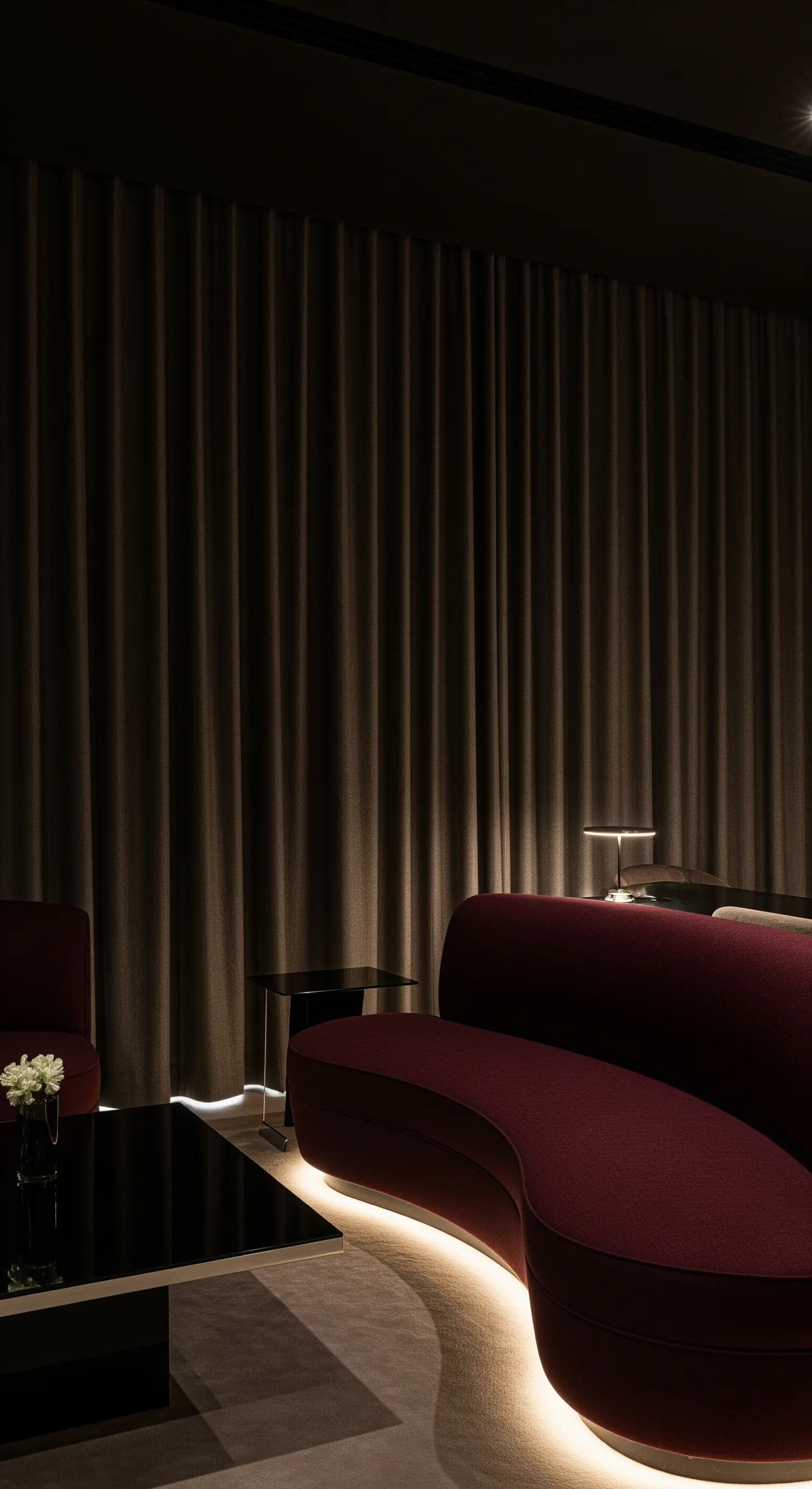 Gebogenes rotes Sofa mit indirekter Bodenbeleuchtung und dunklen Vorhängen
