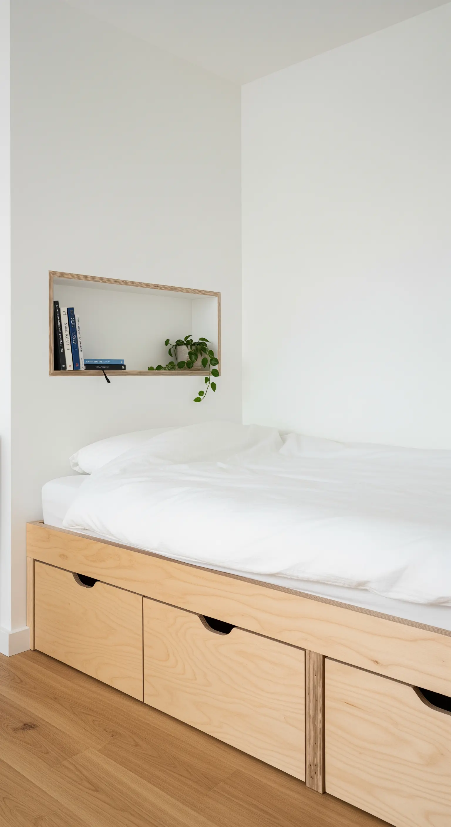 Bett aus hellem Holz mit Schubladen und einer Wandnische für Bücher.