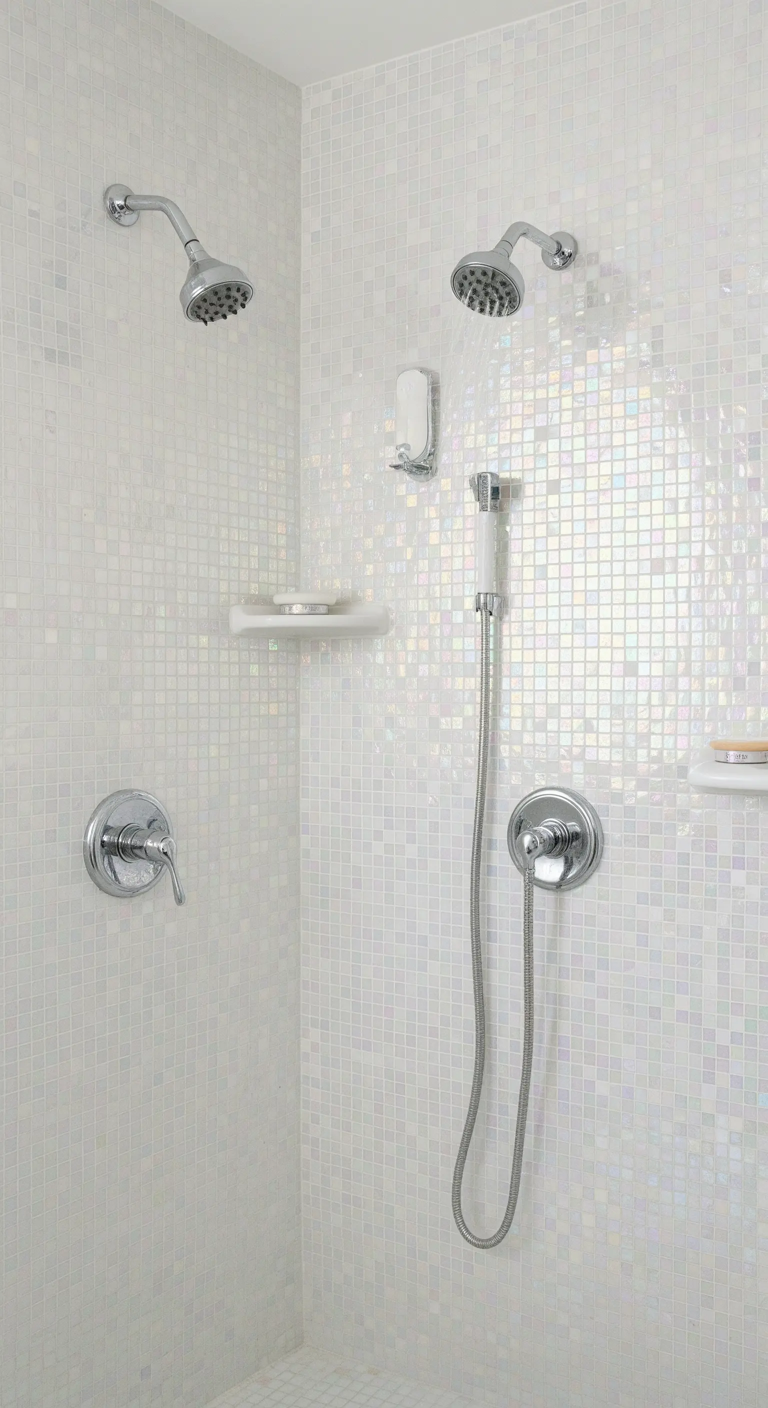 Duschkabine mit weißen, irisierenden Mosaikfliesen, die im Licht schimmern.