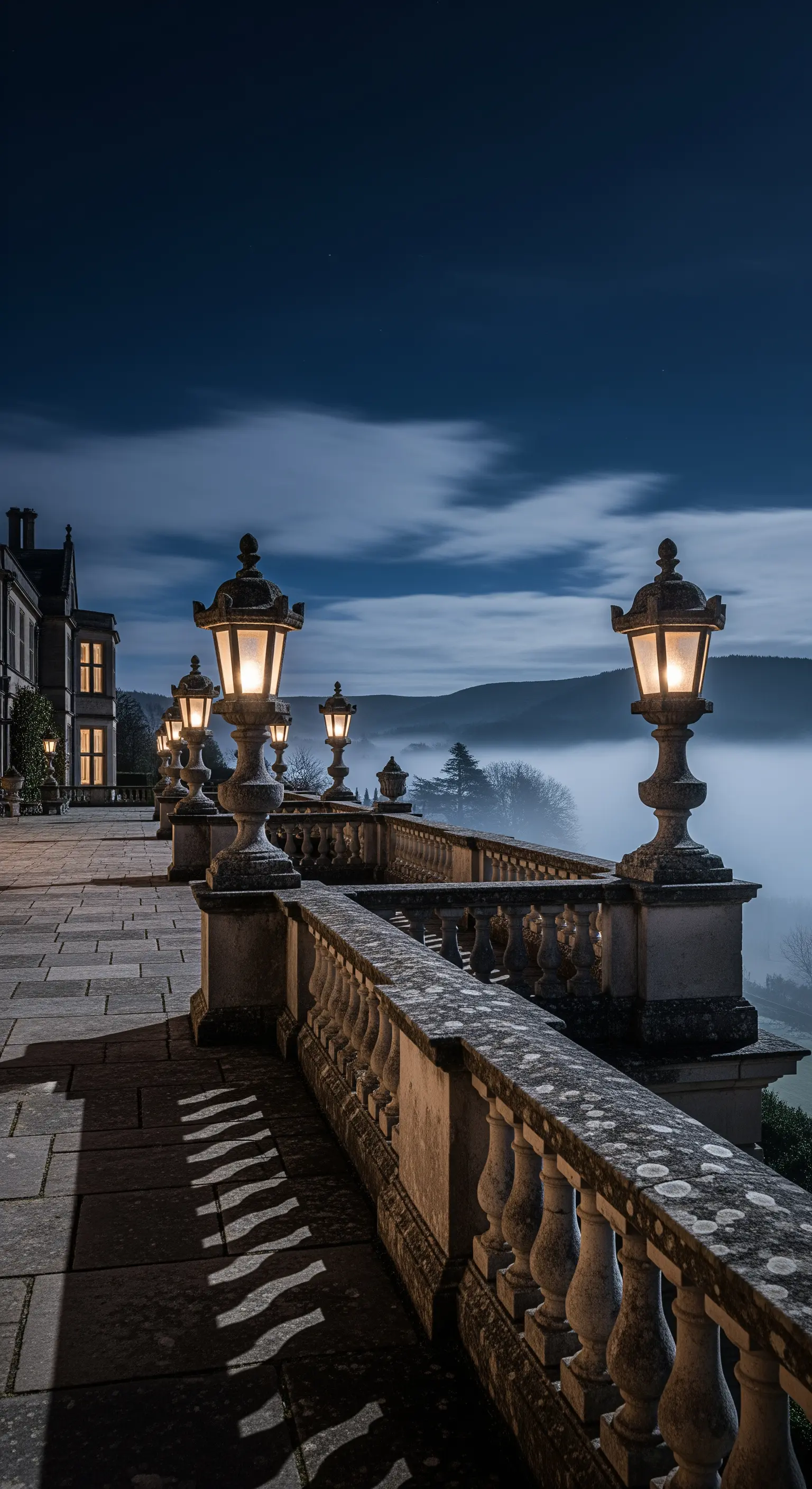 Große Steinterrasse mit klassischen Laternen und weitem Blick in neblige Landschaft.