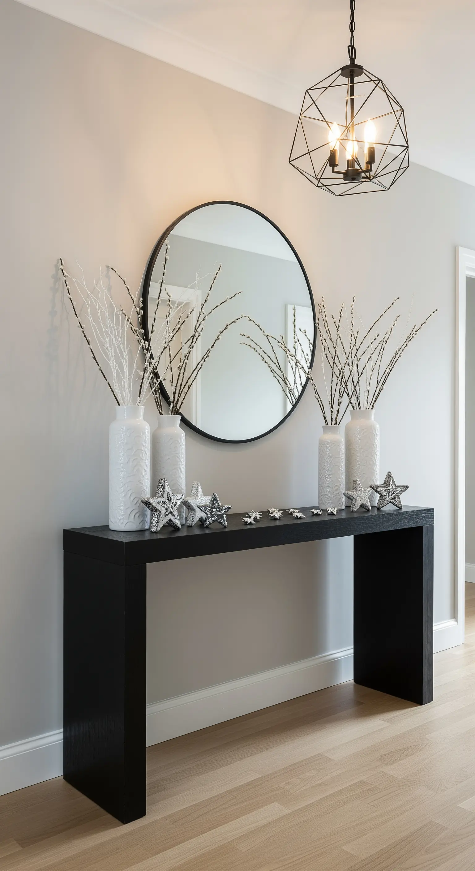 Schwarze Konsole mit weißen Vasen, Ästen, Silbersternen und rundem Spiegel.