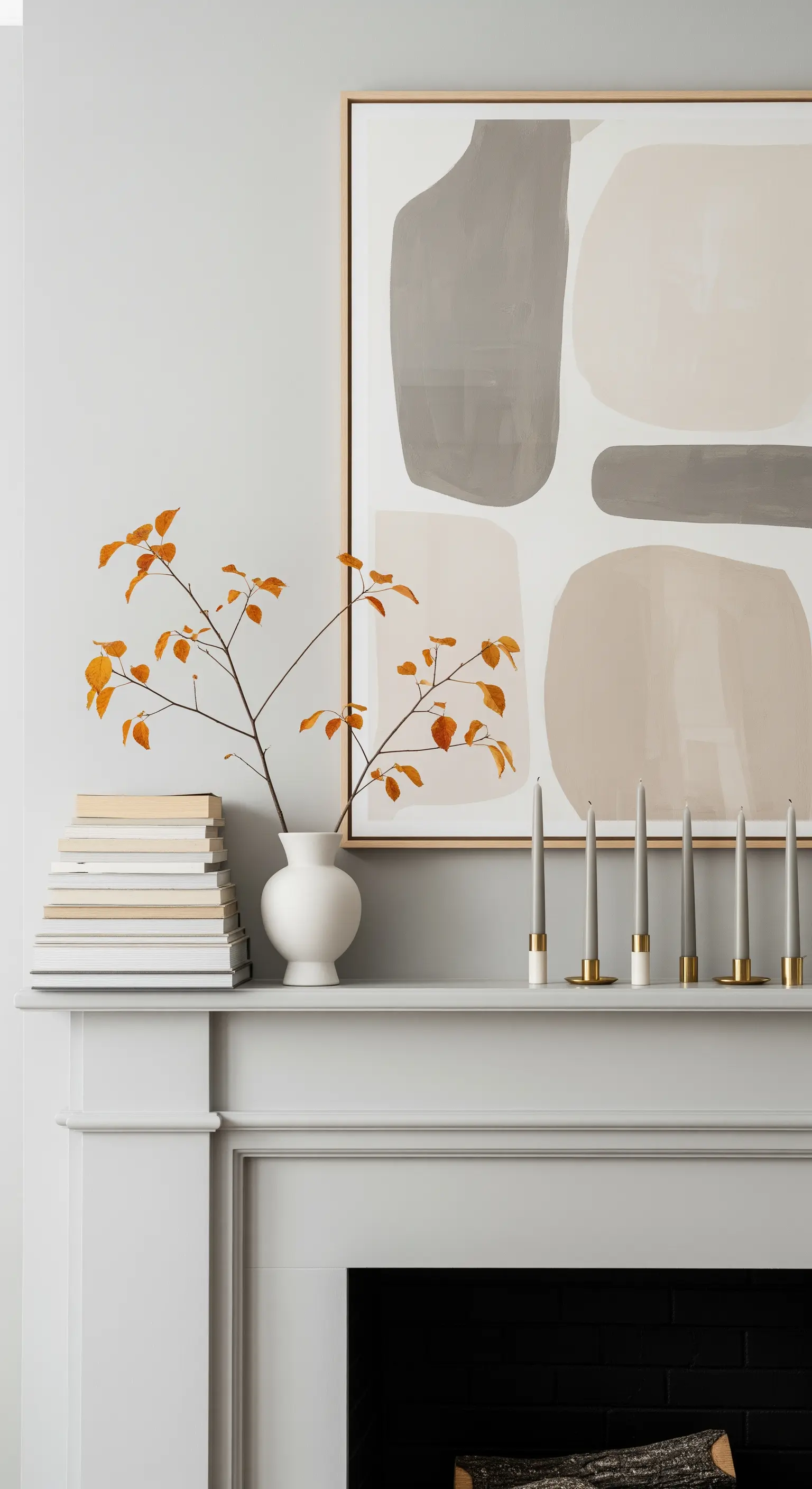 Herbstliche Kaminumrandung mit abstraktem Bild, Büchern, grauen Kerzen und Herbstzweig.