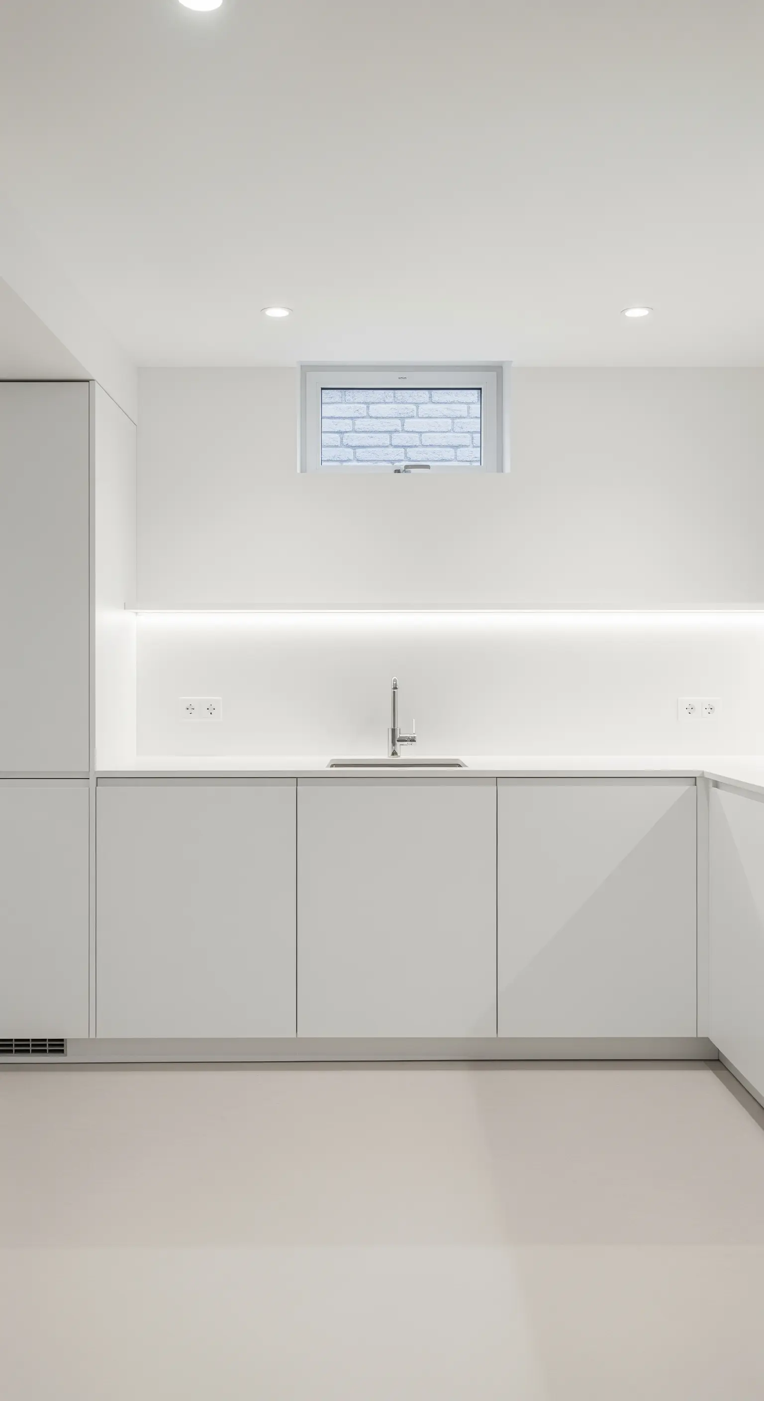Weiße Souterrain-Küche mit einer durchgehenden LED-Lichtleiste als Hauptlichtquelle