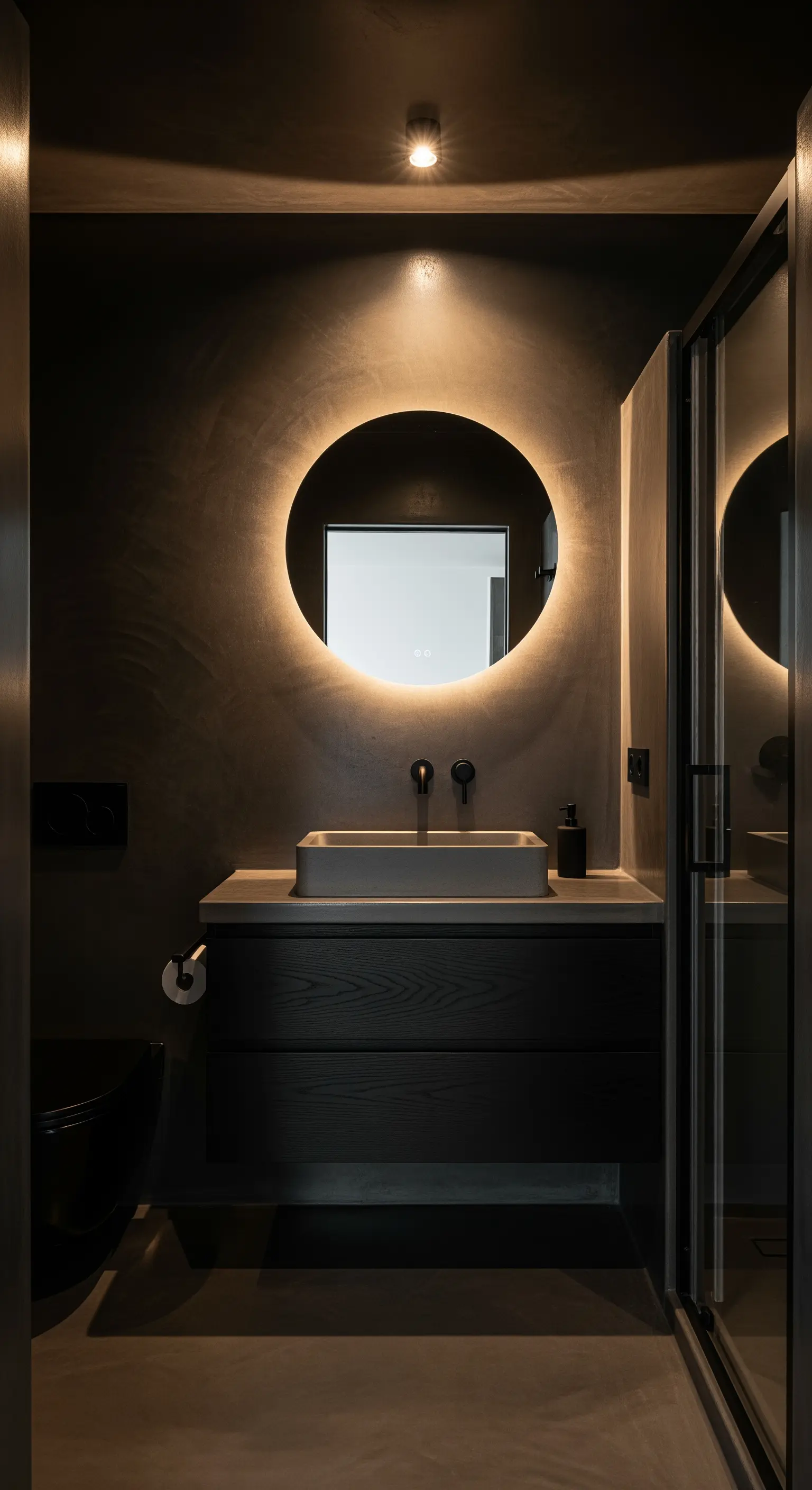Dunkles Badezimmer mit rundem, hinterleuchtetem Spiegel über einem Holzwaschtisch.