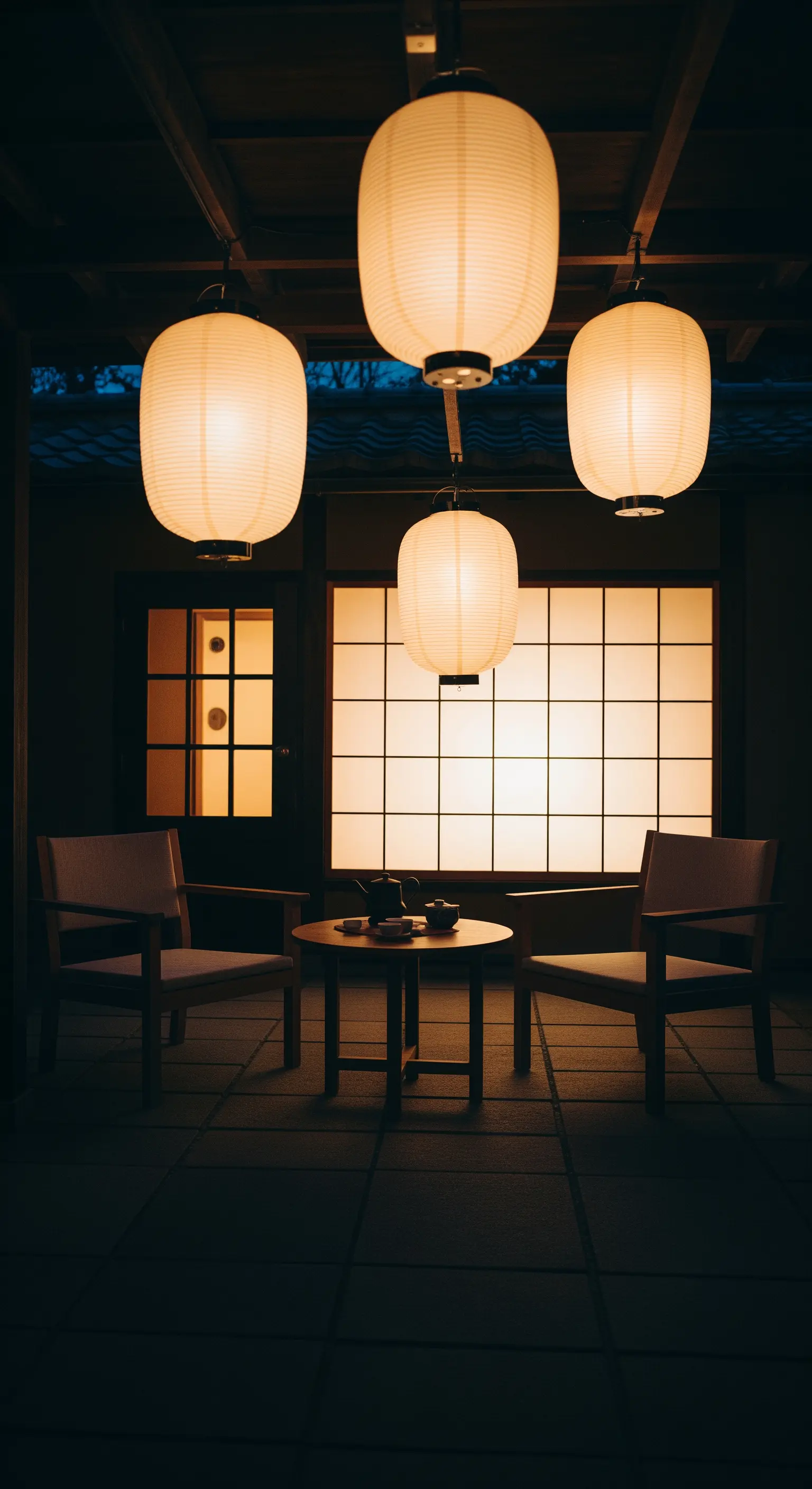 Abendliche Teeecke mit leuchtenden japanischen Papierlaternen vor einer Shoji-Wand