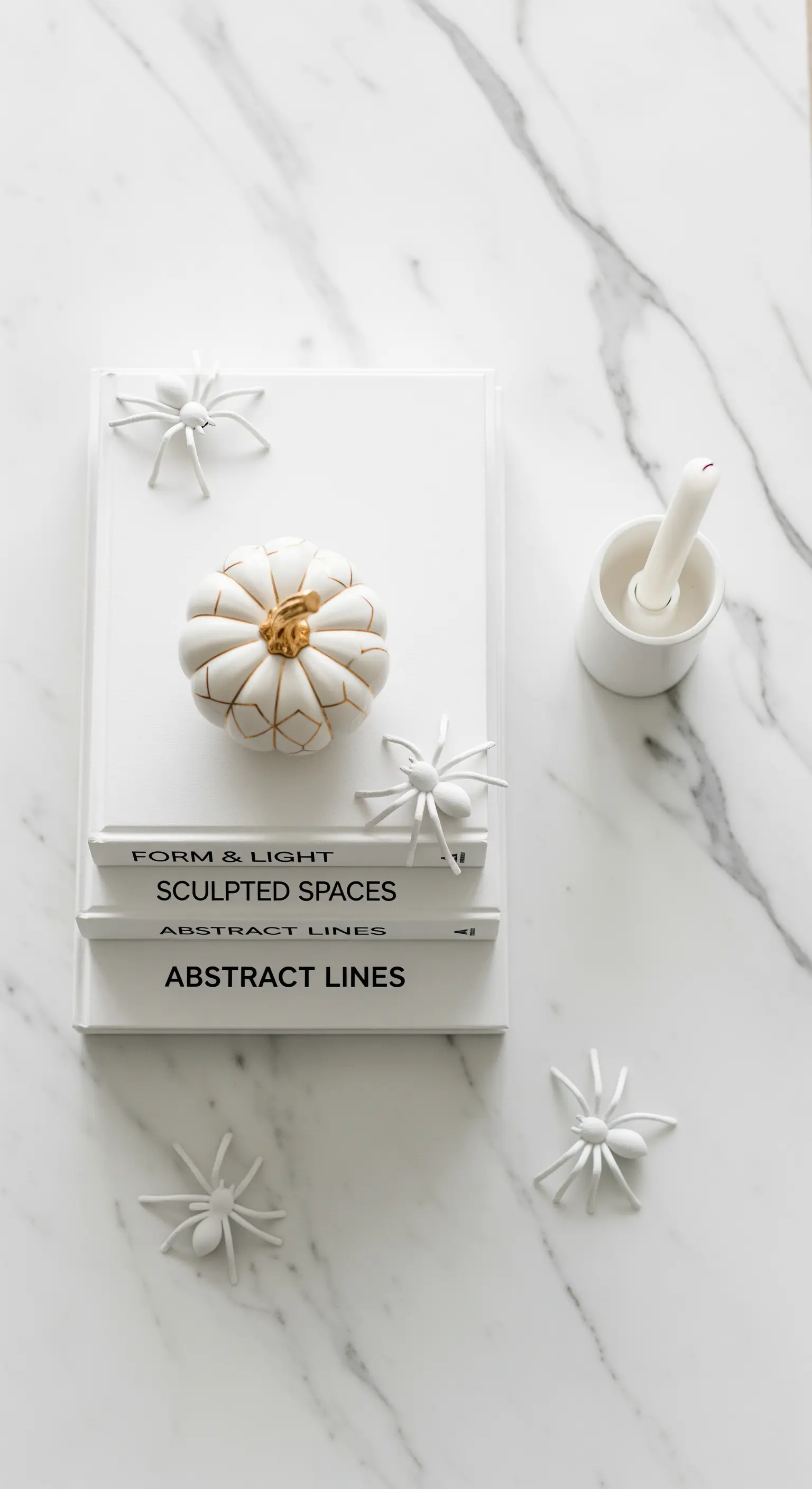 Marmorfläche mit weißen Büchern, goldenem Kürbis und weißen Spinnen