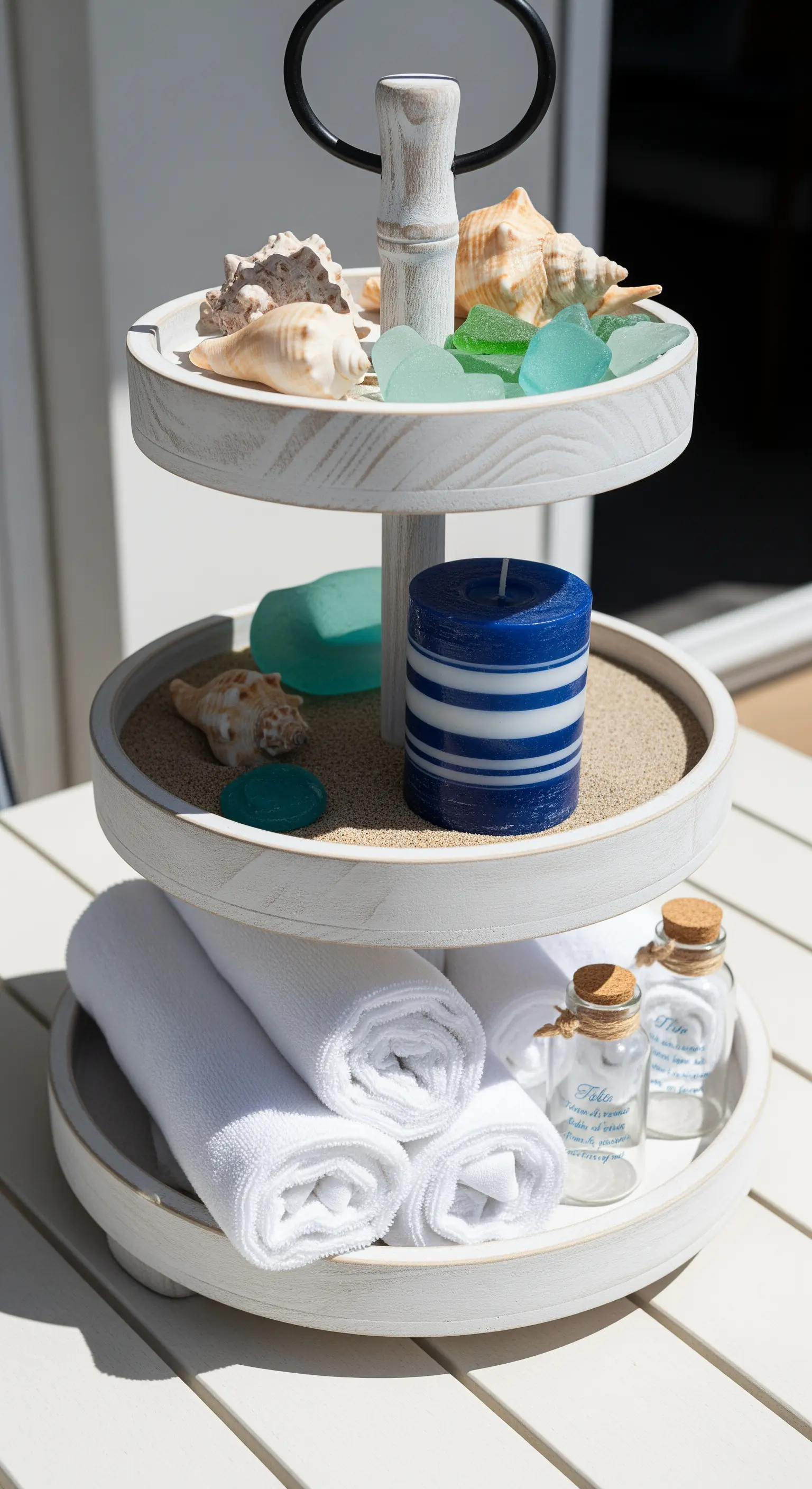 Weiße Etagere mit Muscheln, Sand, Kerze und Handtüchern im maritimen Stil