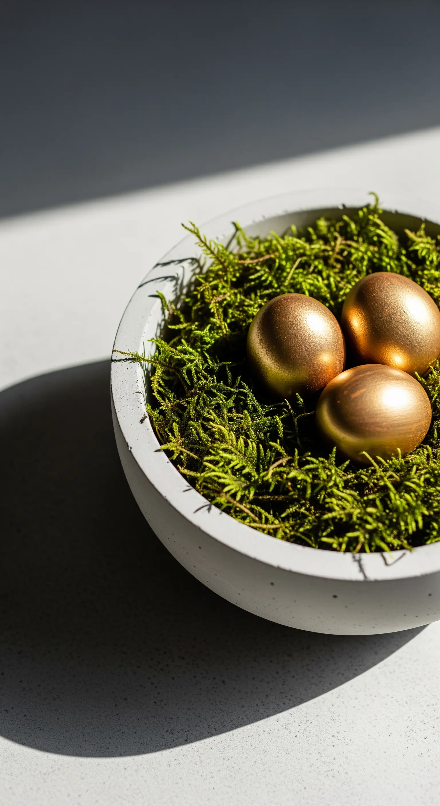 Graue Betonschale mit Moos und drei goldenen Ostereiern