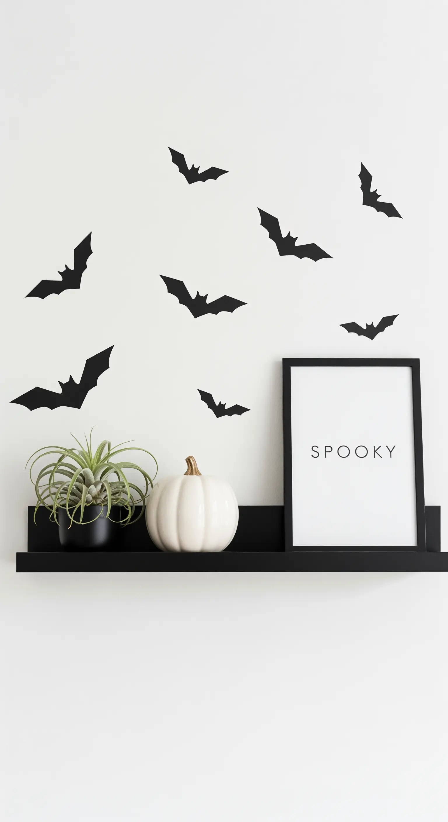 Minimalistische schwarze Fledermaus-Wandsticker über einem schwarzen Regal mit weißem Kürbis.