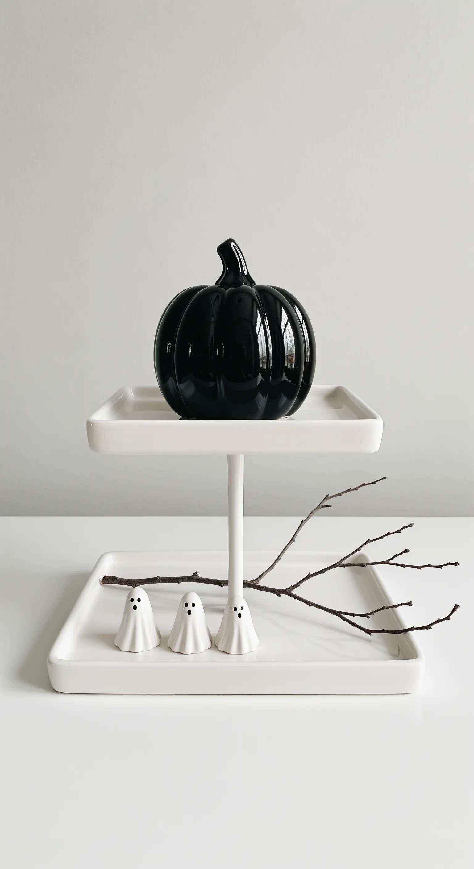 Minimalistische Halloween-Deko auf weißer Etagere mit schwarzem Kürbis.