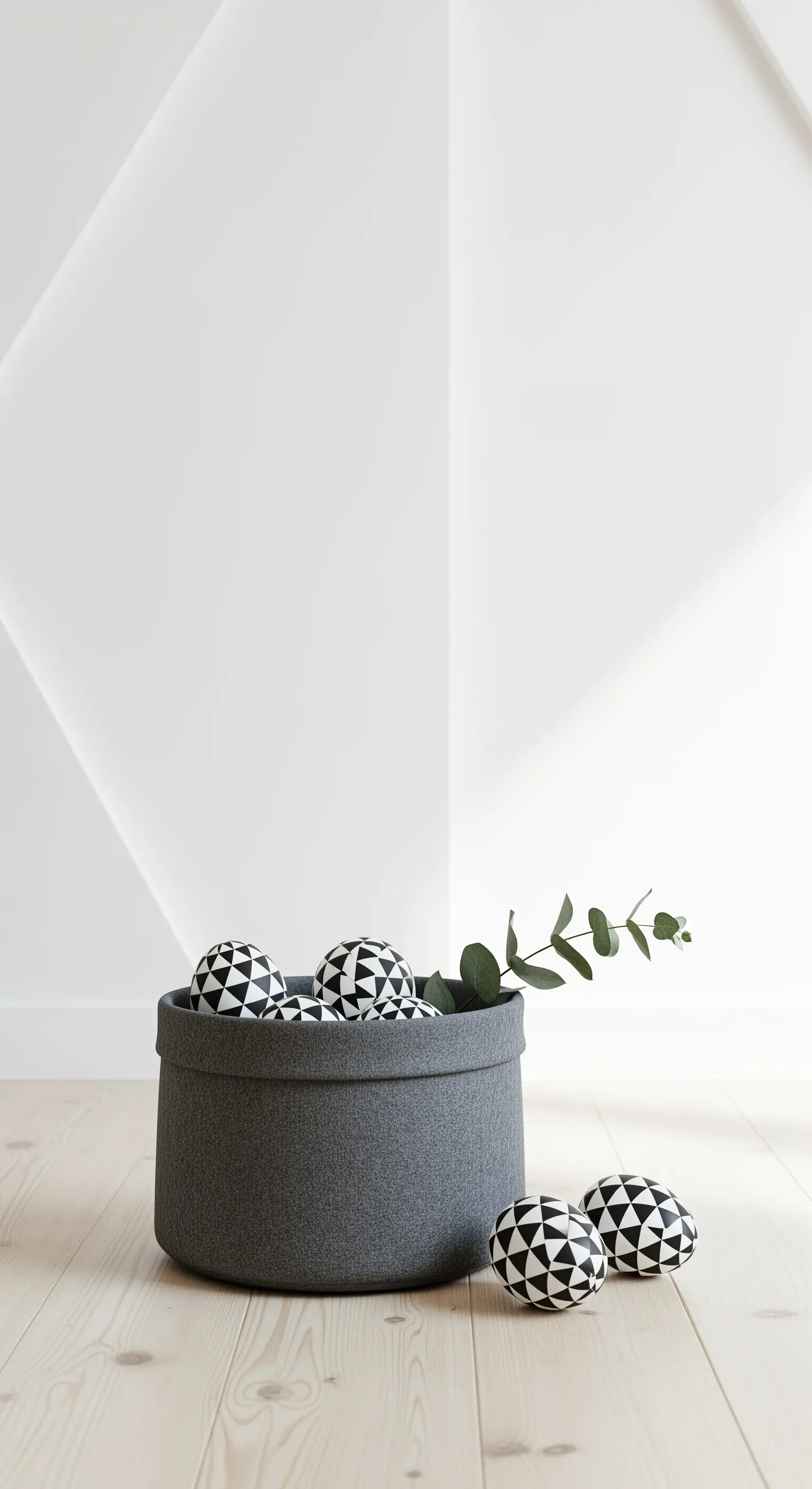 Grauer Filzkorb mit schwarz-weißen geometrischen Eiern und Eukalyptuszweig in minimalistischem Raum