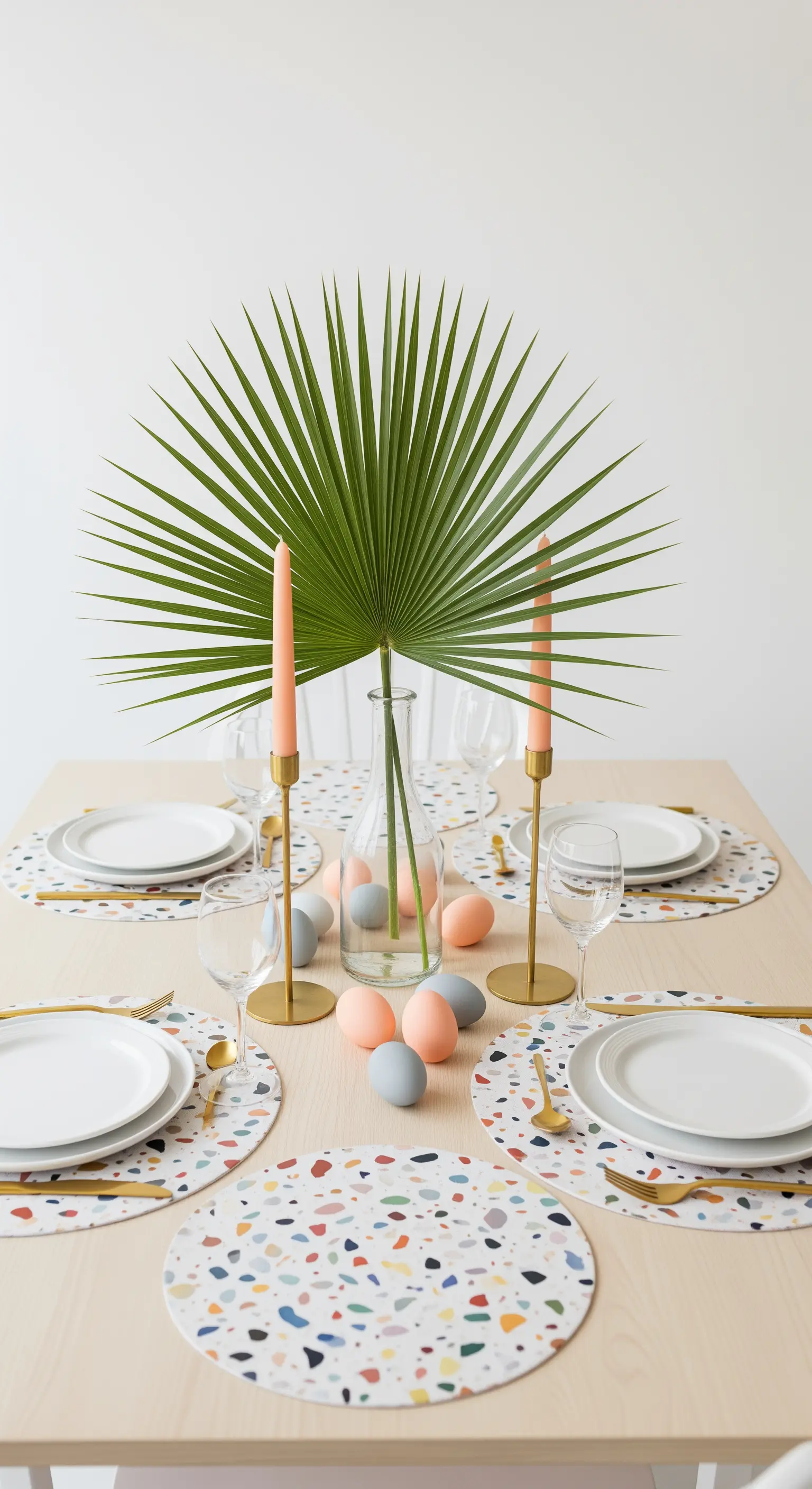 Moderne Ostertafel mit Terrazzo-Platzsets, Palmenblatt und pastellfarbenen Akzenten.