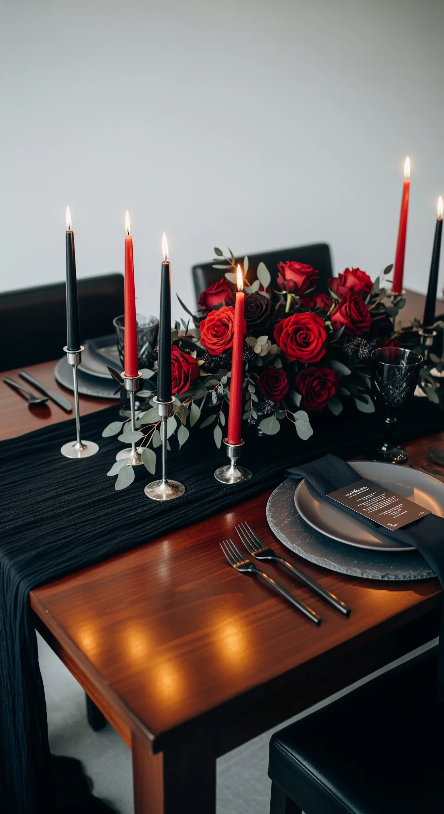 Dramatische Tischdeko mit schwarzen und roten Stabkerzen und roten Rosen.