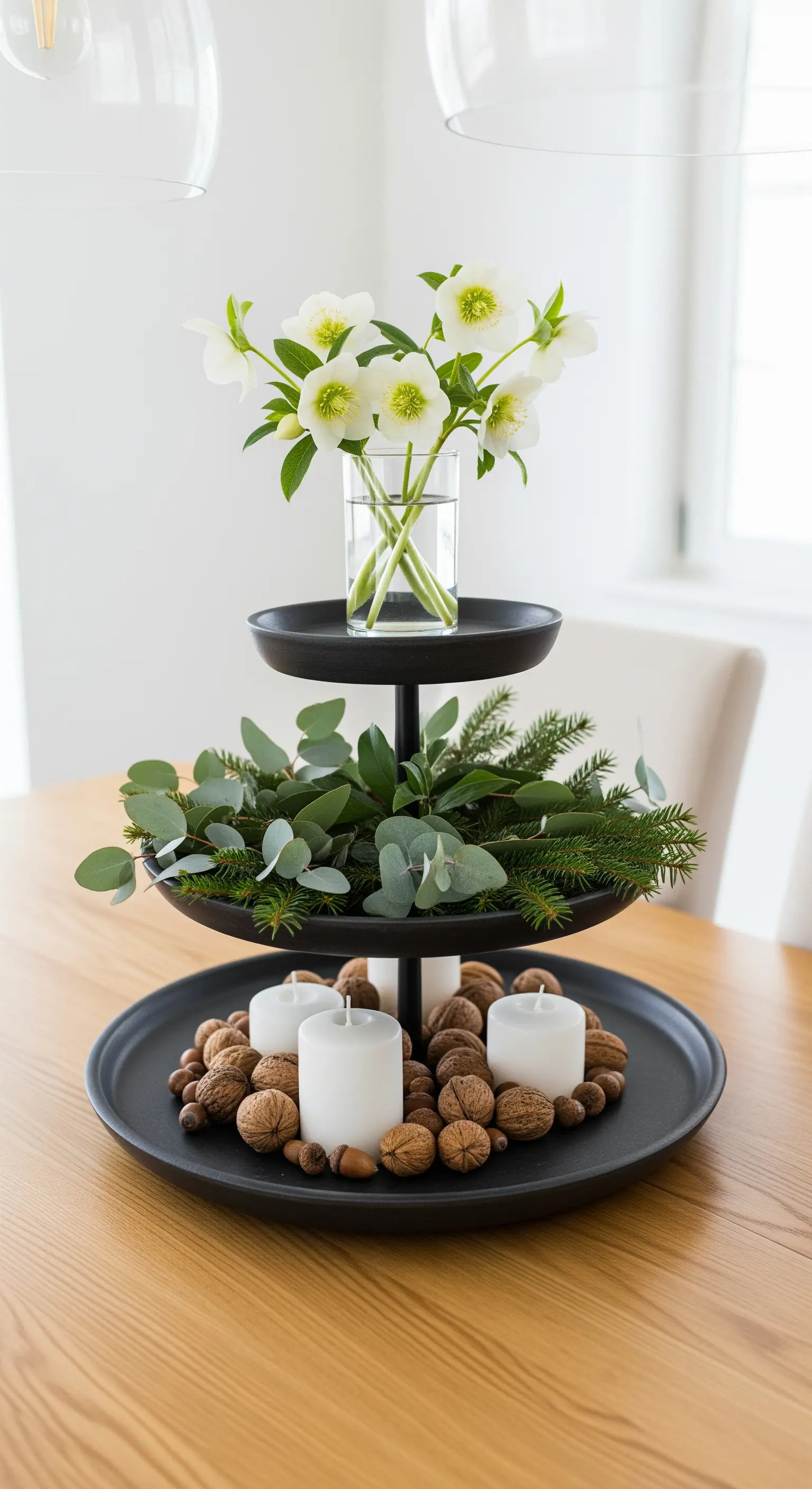 Schwarze Etagere mit Christrosen, Eukalyptus, Walnüssen und weißen Kerzen.