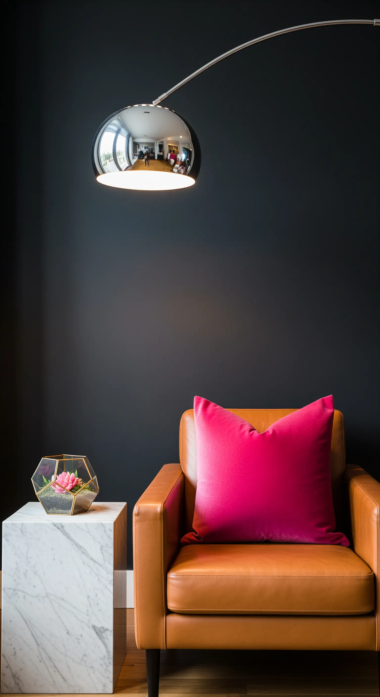 Cognacfarbener Ledersessel vor einer schwarzen Wand mit einem pinken Kissen und Marmortisch.