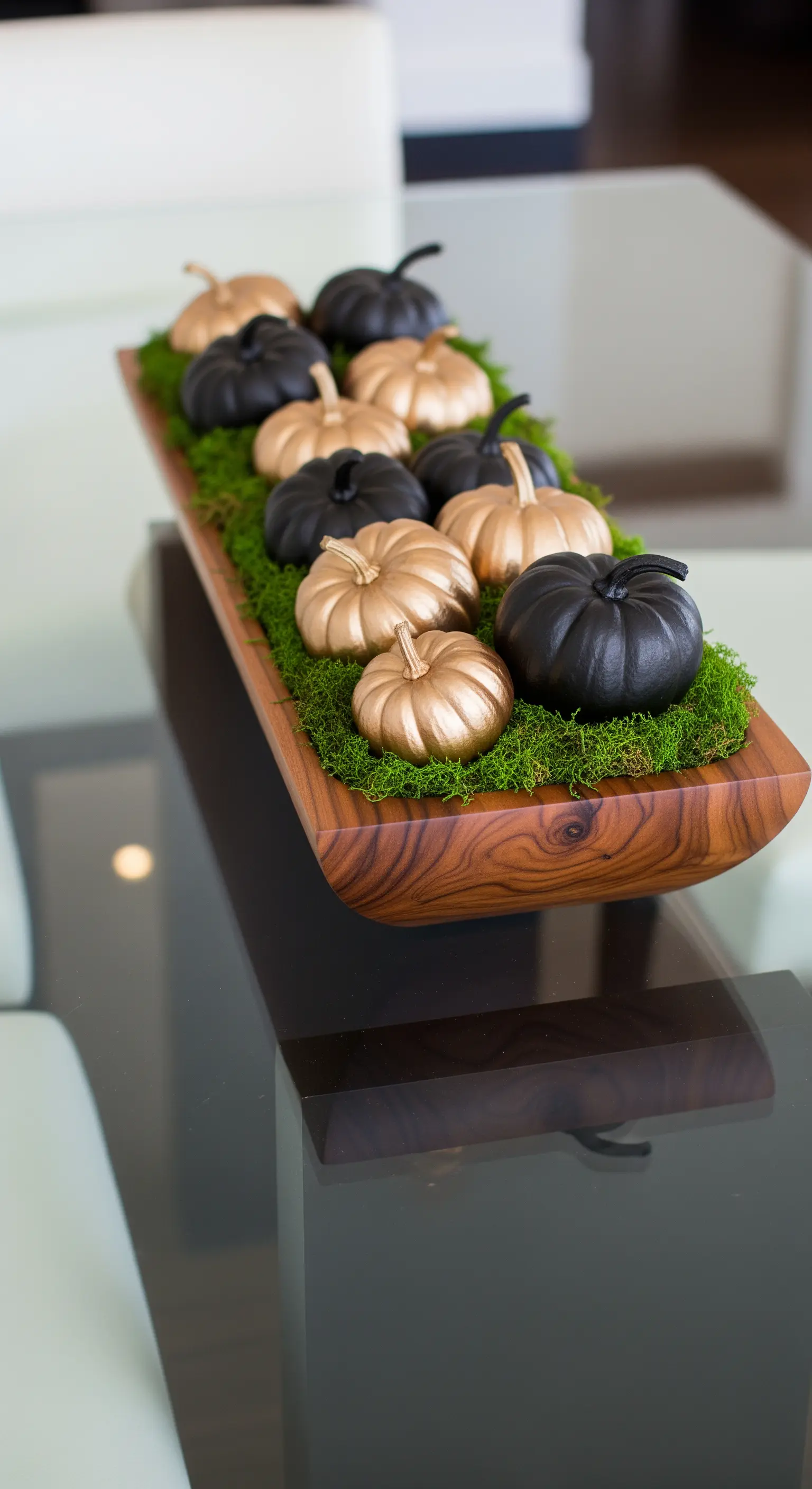 Holztisch mit schwarzen und goldenen Kürbissen auf Moos in einer Schale.