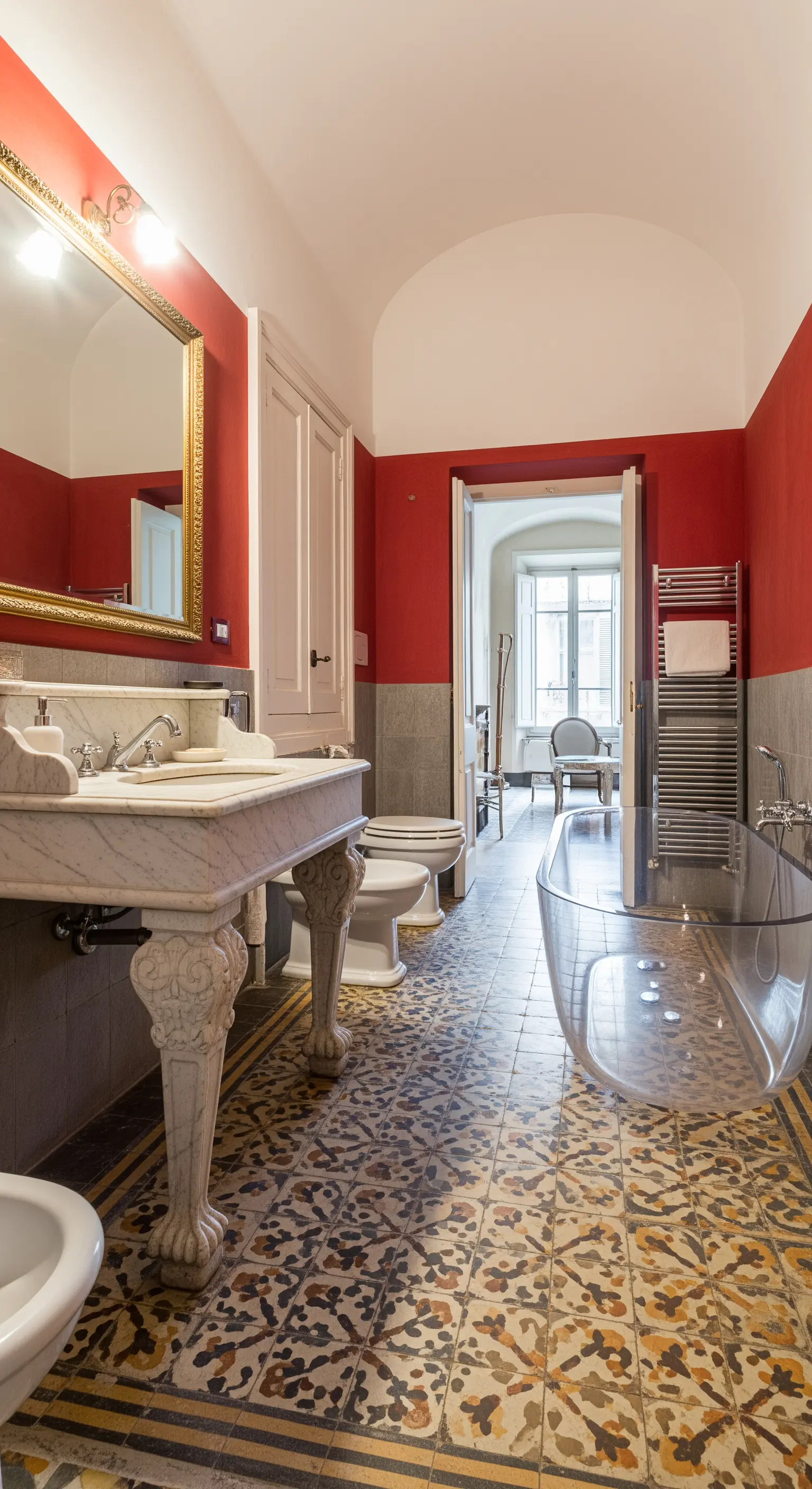 Opulentes Badezimmer mit roten Wänden, Ornamentfliesen und einer modernen transparenten Badewanne.