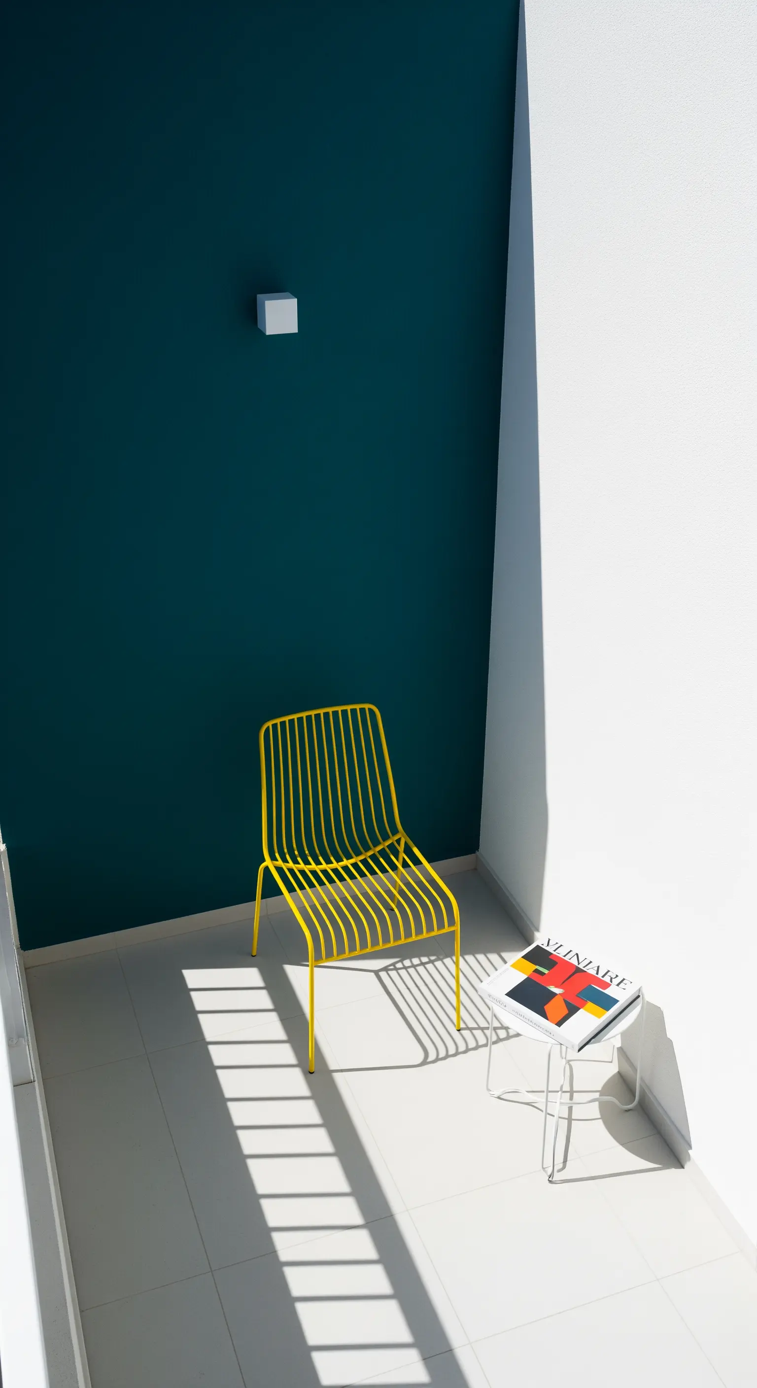Dunkelgrüne Wand mit gelbem Drahtstuhl und grafischem Schatten