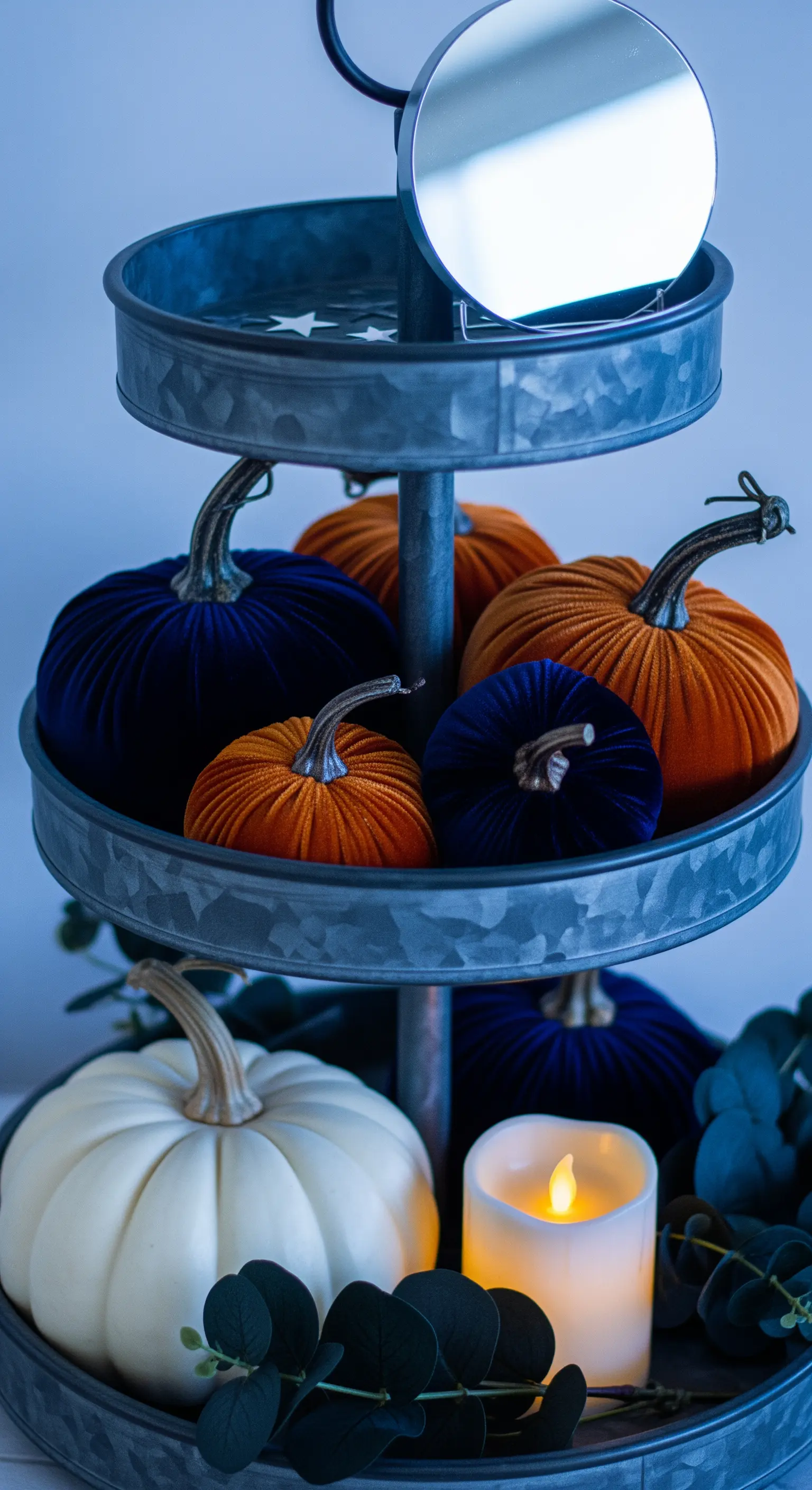 Etagere mit blauen und orangen Samtkürbissen und einer Kerze