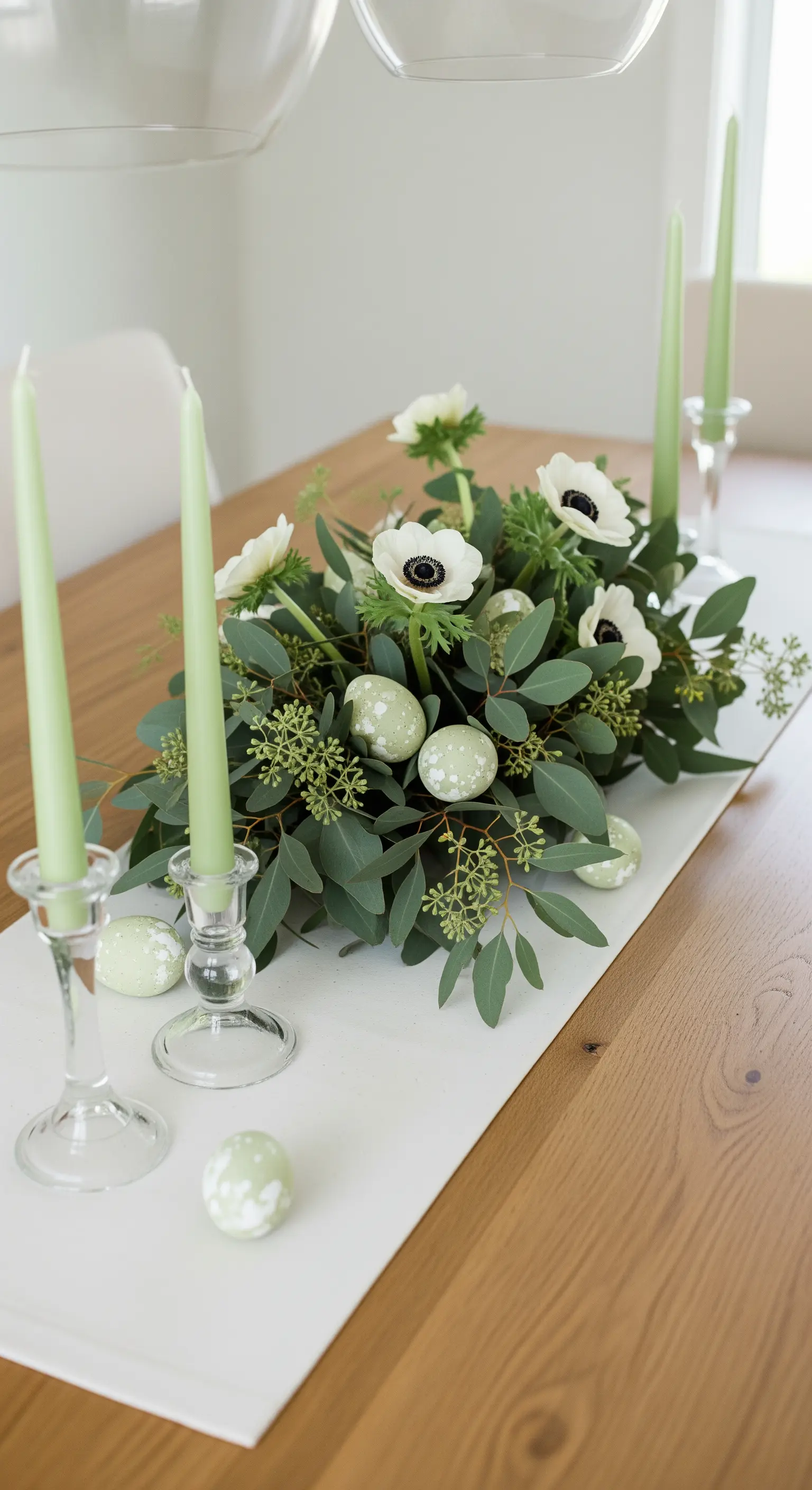 Tischmitte mit Eukalyptus, Anemonen, grünen Kerzen und gesprenkelten Ostereiern.
