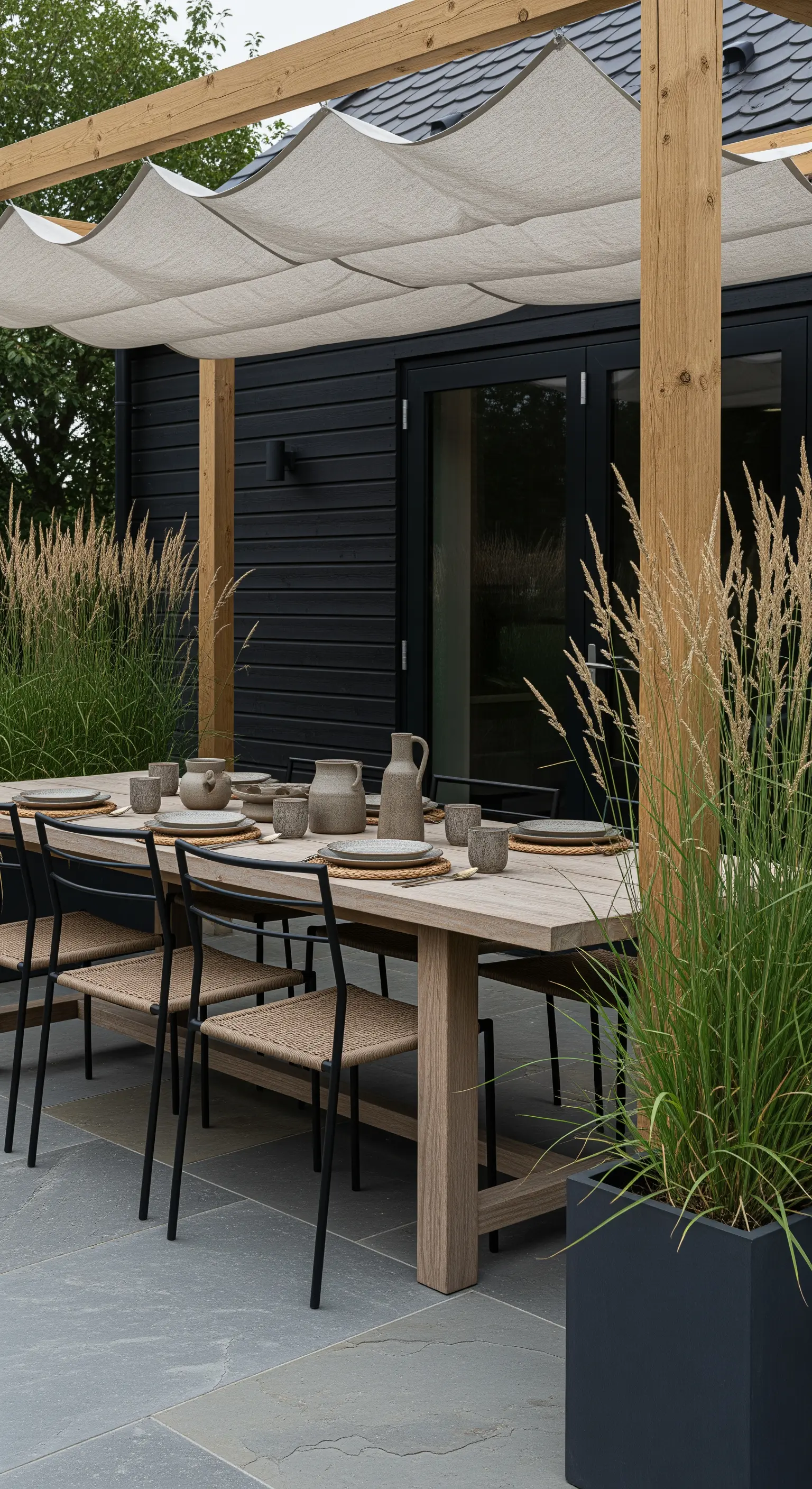 Japandi-Essbereich im Freien mit Holztisch, schwarzen Stühlen und Ziergräsern unter einem Sonnensegel