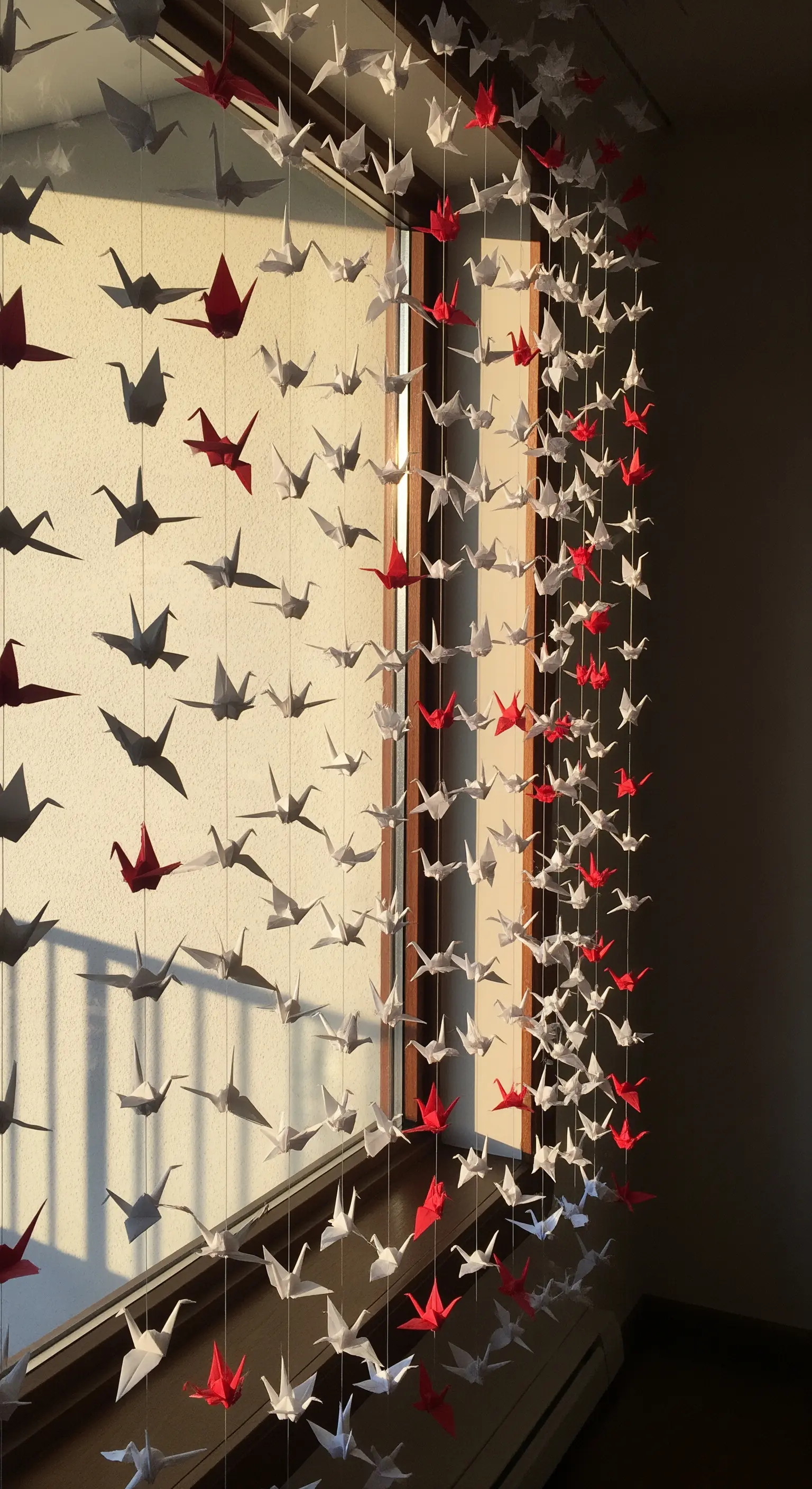 Fenster mit hängendem Vorhang aus weißen, grauen und roten Origami-Kranichen.