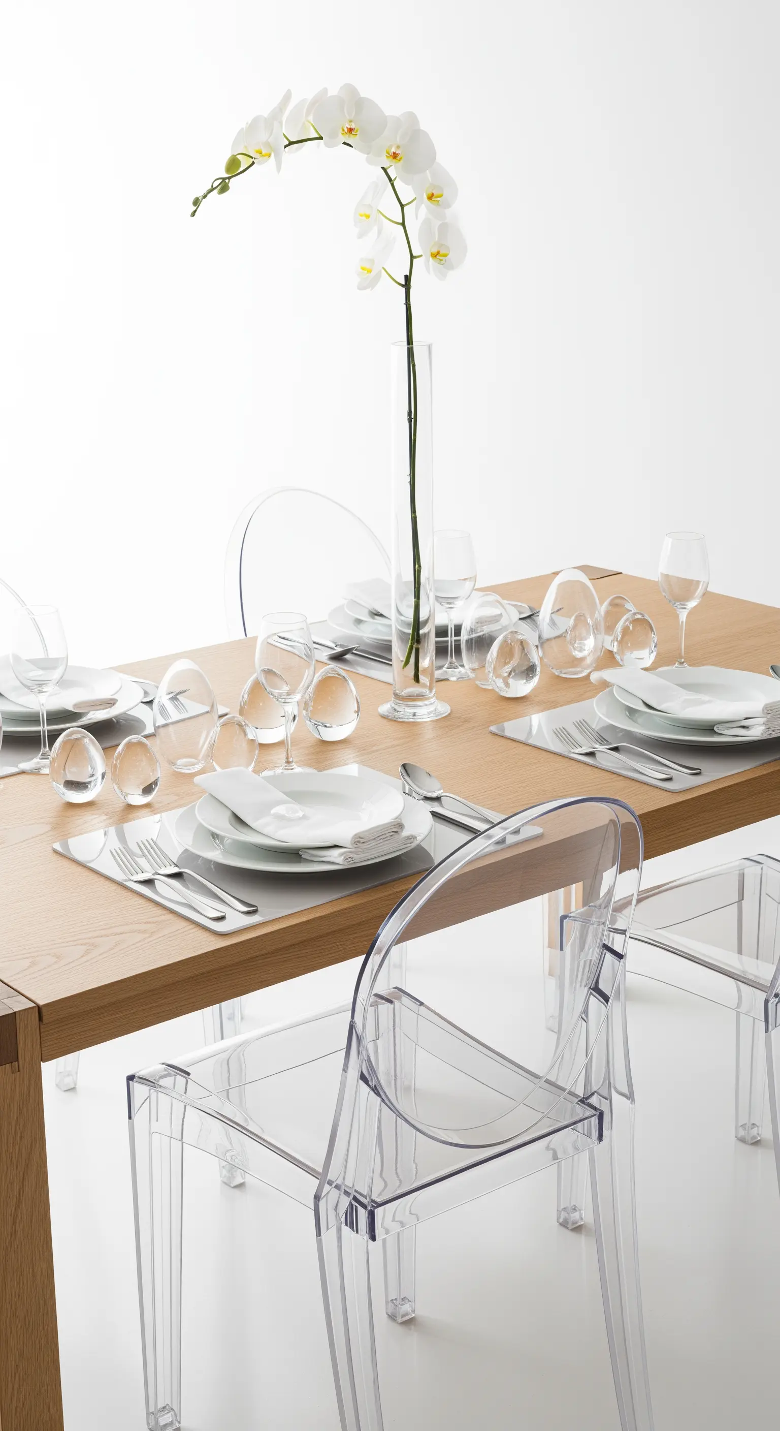 Minimalistischer Ostertisch mit einem einzelnen Orchideenstiel und transparenten Stühlen.