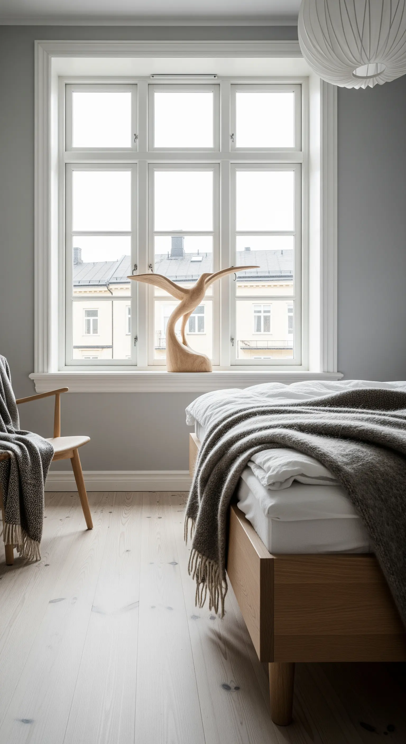 Helle Holzskulptur auf einer Fensterbank in einem minimalistischen skandinavischen Schlafzimmer.