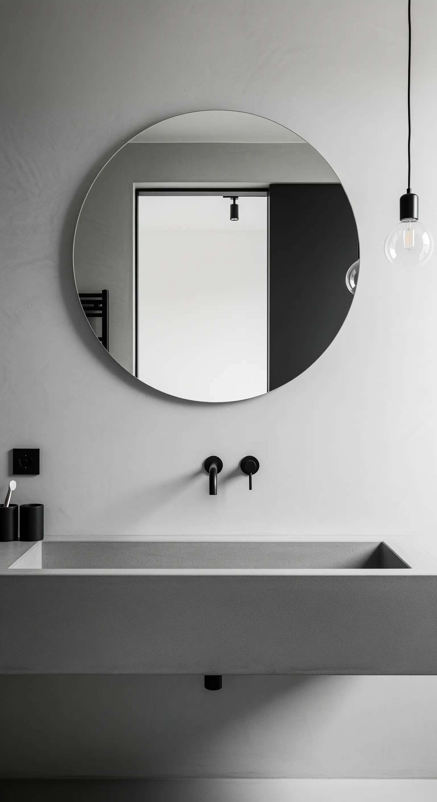 Minimalistischer Betonwaschtisch mit rundem Spiegel und schwarzen Armaturen.