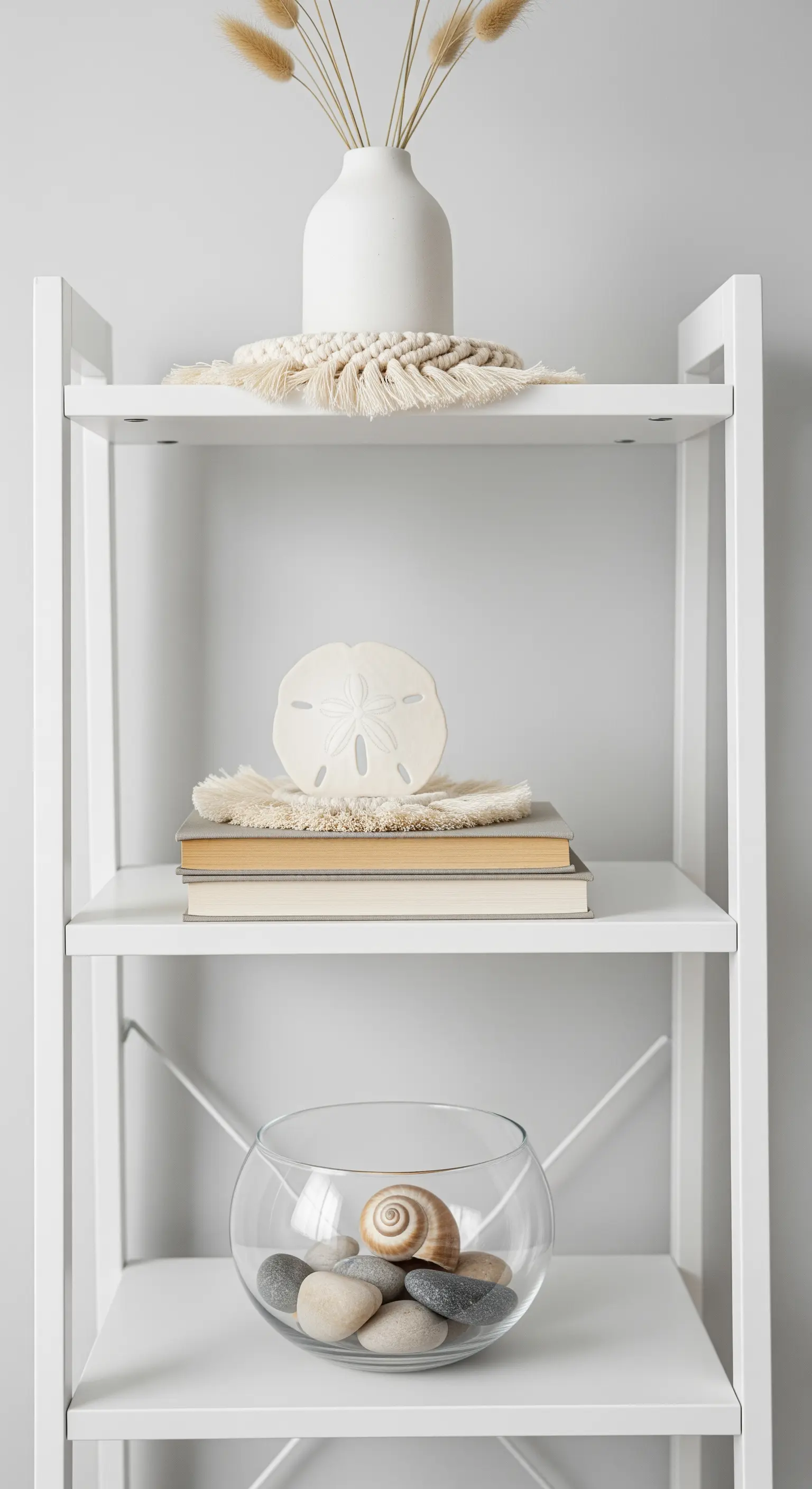 Weißes Regal mit minimalistischer Deko aus Sanddollar, Steinen und Trockenblumen.
