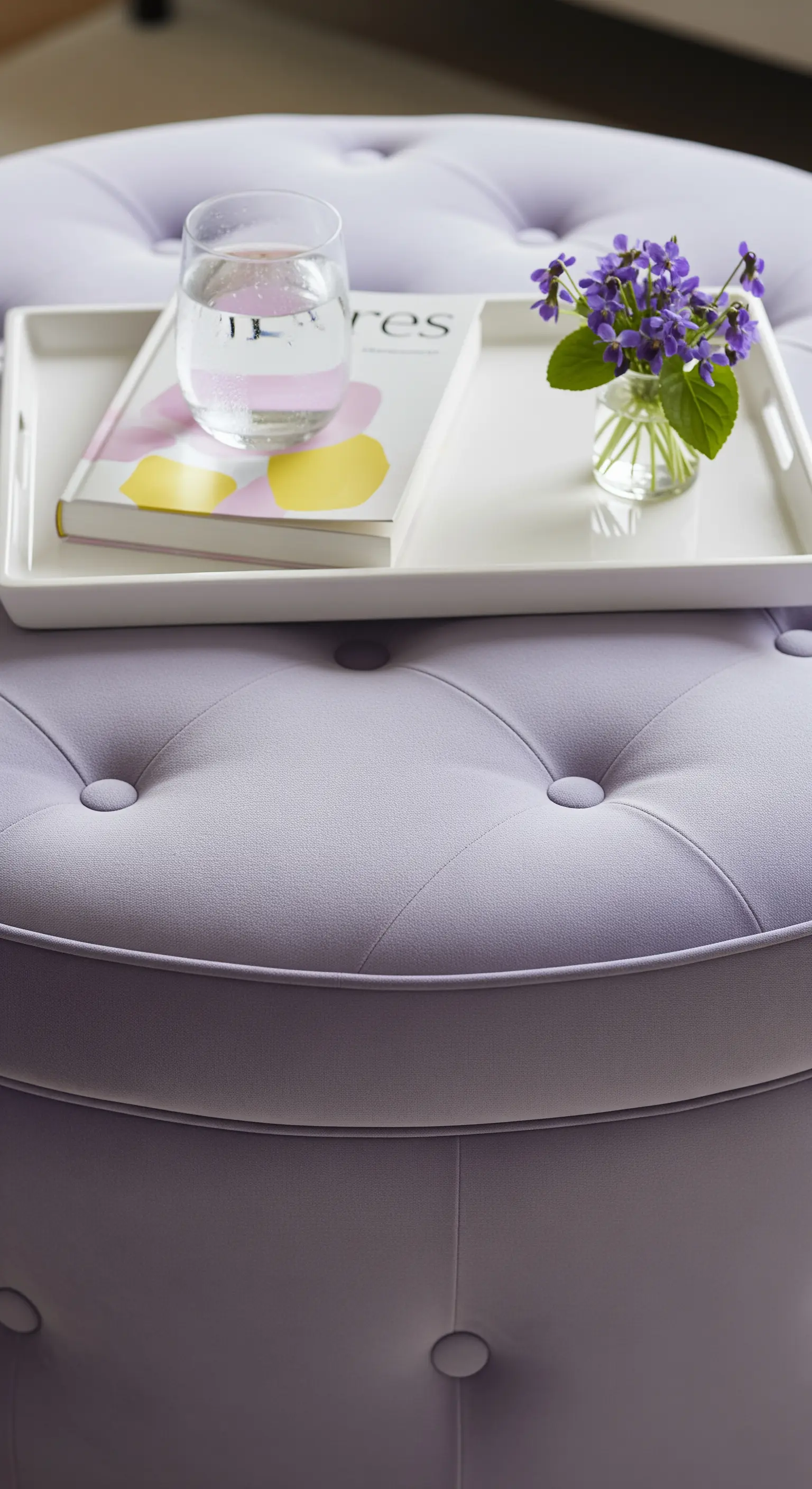 Lavendelfarbener Pouf mit Tablett, Buch, kleiner Vase mit Veilchen