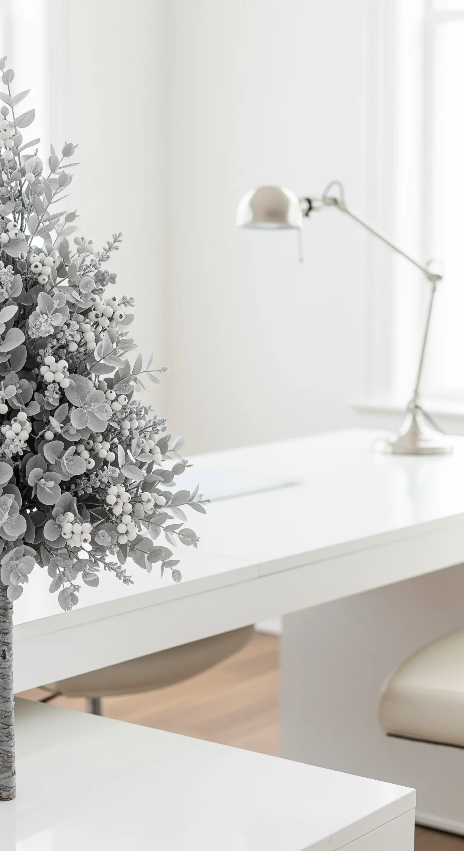 Minimalistische silbergraue Kunstpflanze auf einem weißen Schreibtisch mit Lampe.