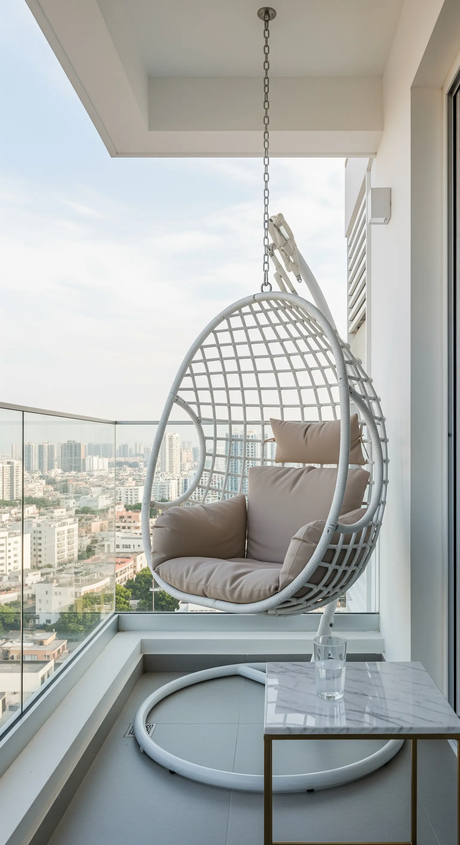 Weißer Hängesessel auf Balkon mit Glasgeländer und Stadtblick
