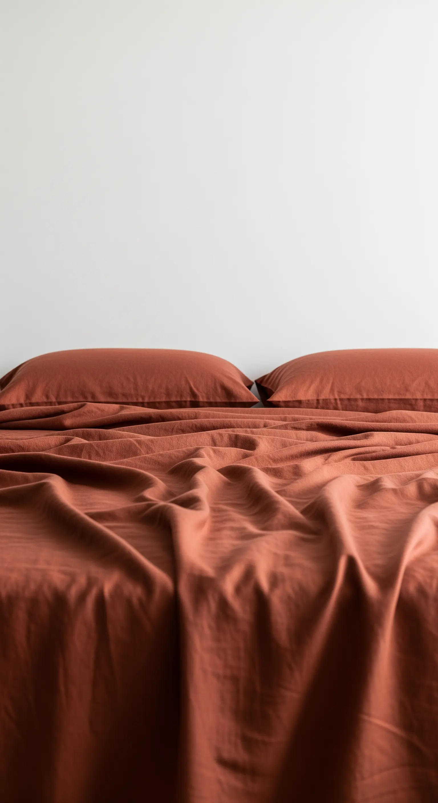 Ein Bett, komplett bezogen mit unifarbener Bettwäsche in einem warmen Terrakotta-Ton.