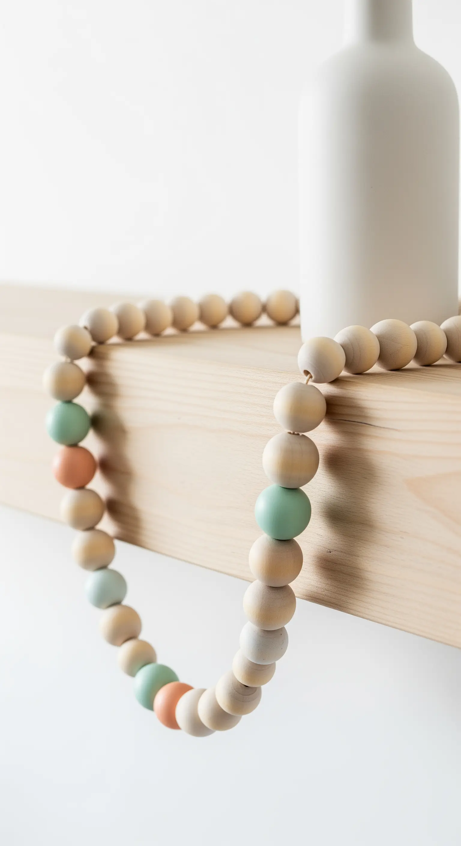 Holzperlen-Girlande mit pastellfarbenen Akzenten auf einem Holzbalken.