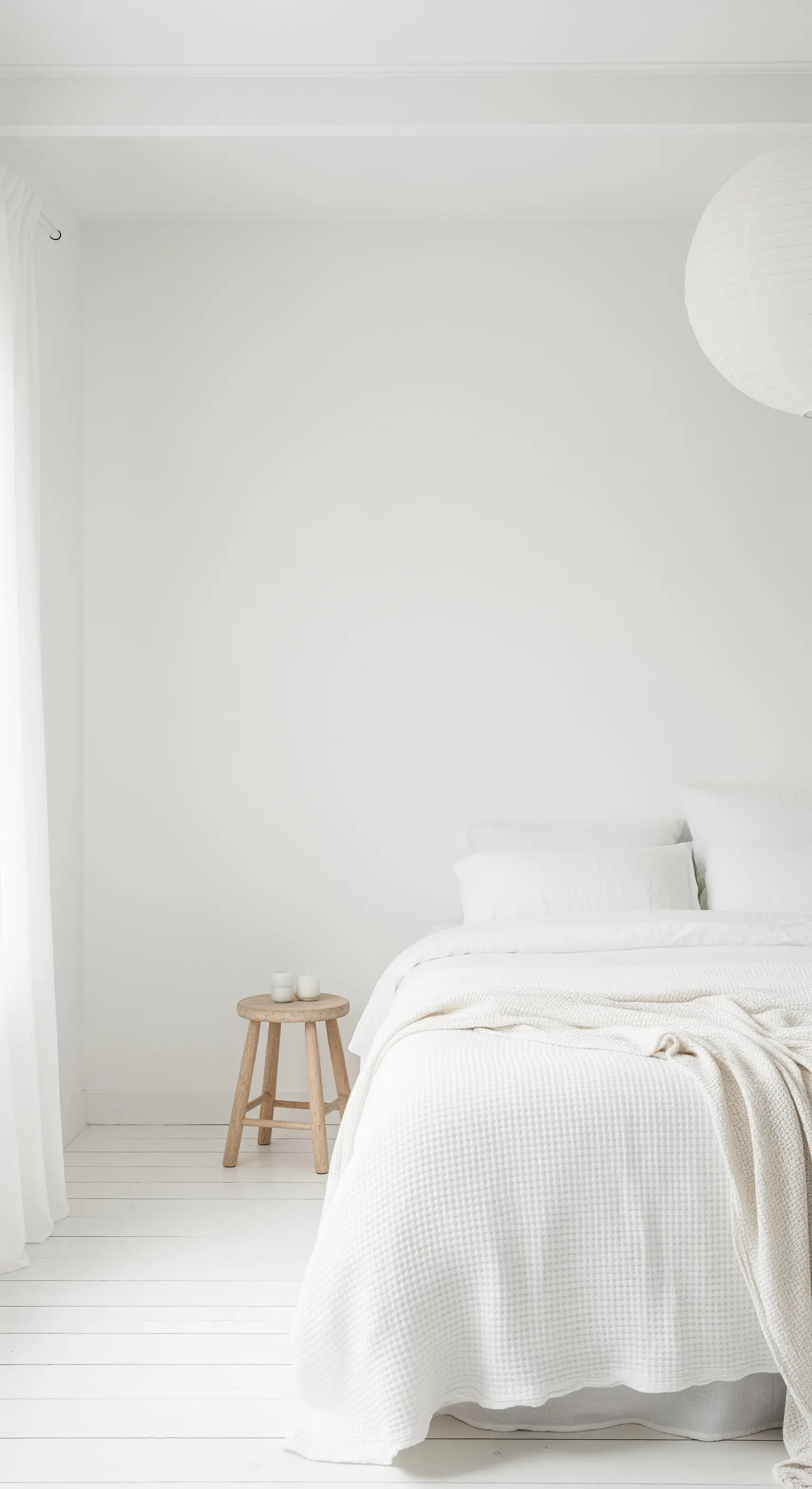 Ganz in Weiß gehaltenes Schlafzimmer mit einem Holzhocker neben dem Bett.