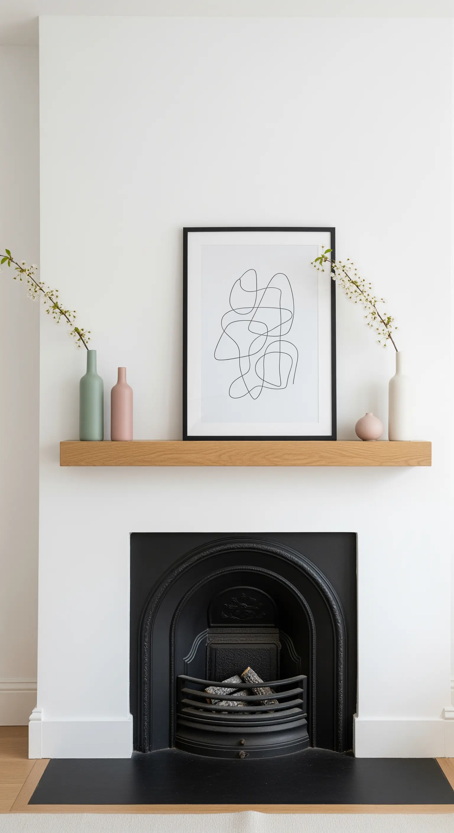 Minimalistische Kamin-Deko mit blühenden Zweigen in Pastellvasen und Kunstdruck.