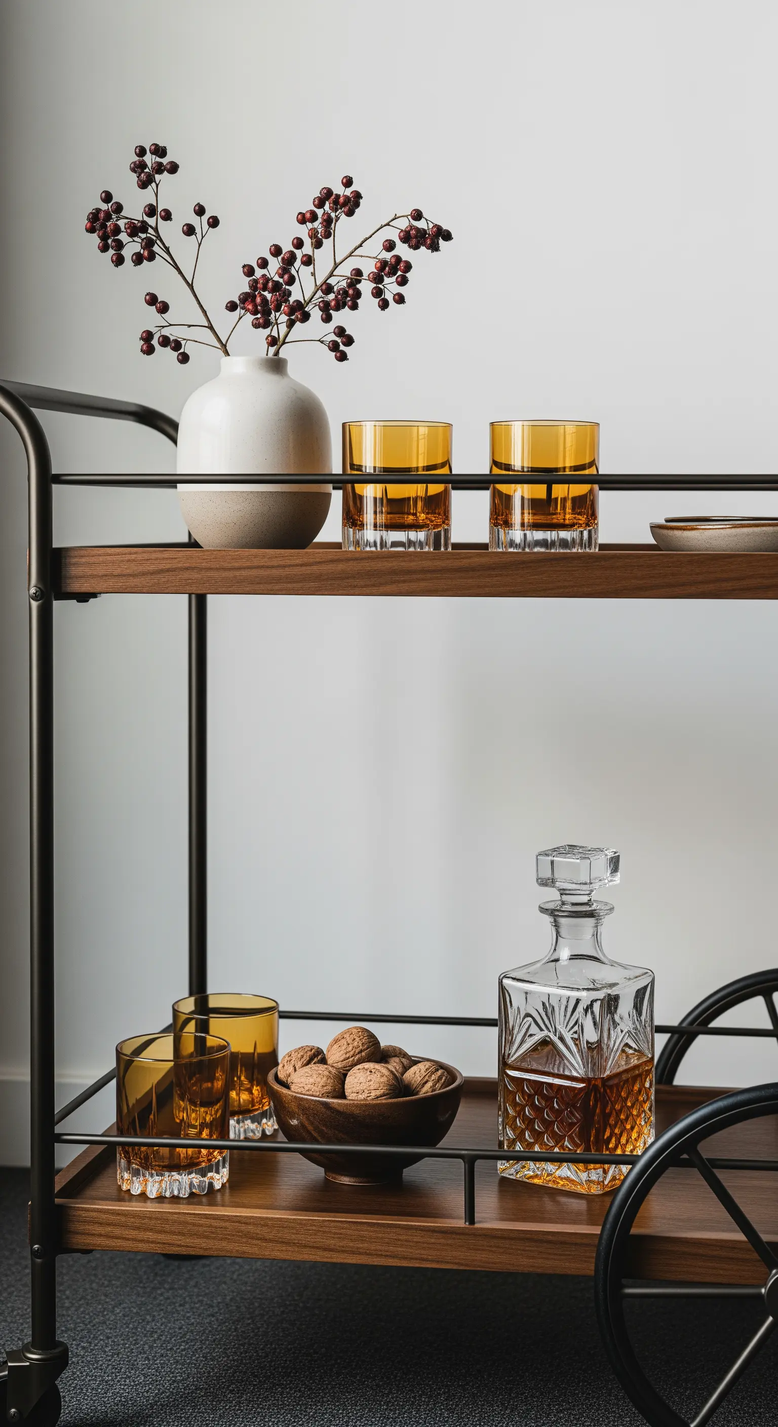 Barwagen mit Whiskey-Karaffe, bernsteinfarbenen Gläsern und einer Vase mit roten Beeren.