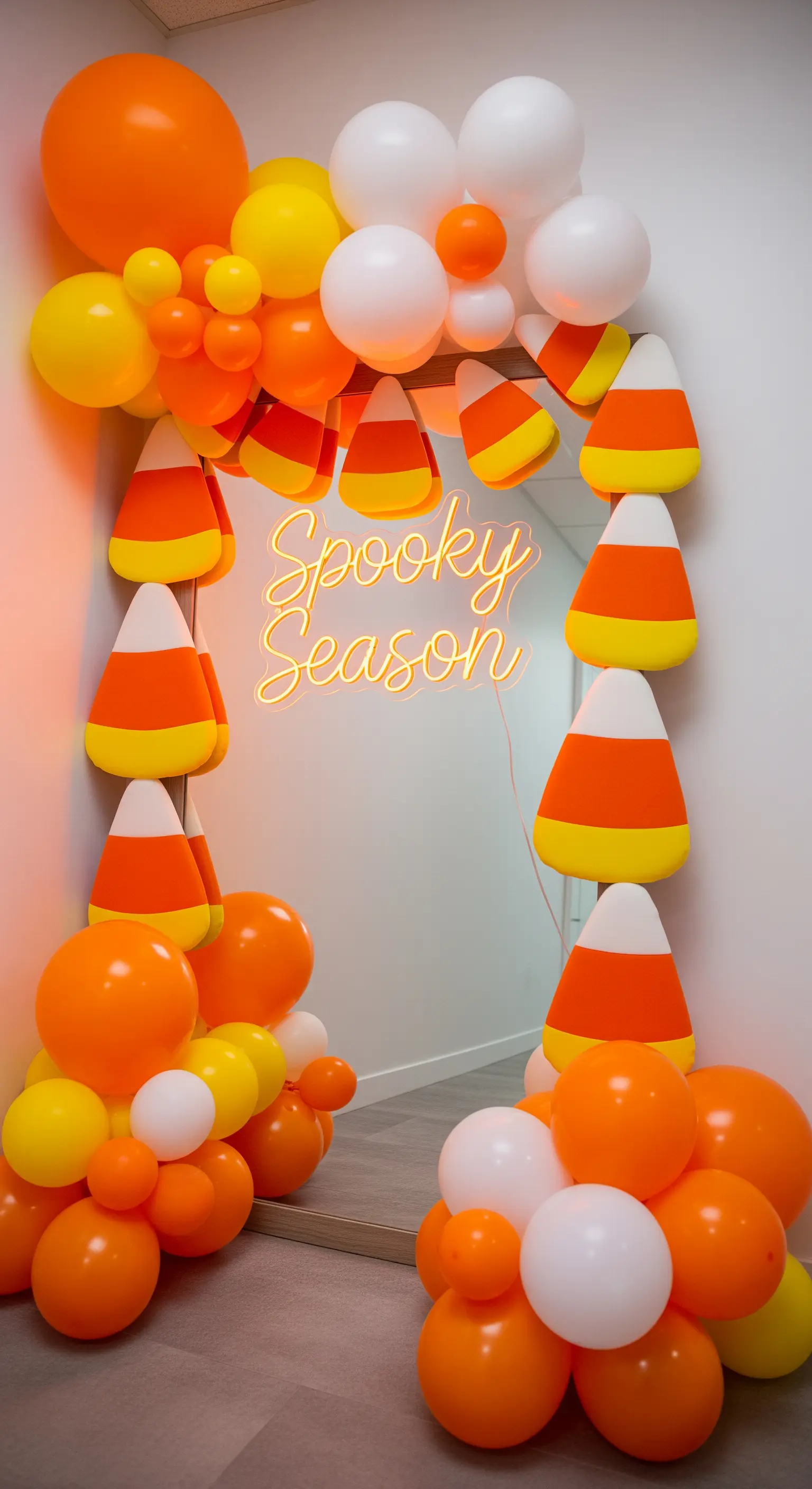 Standspiegel umrahmt von Candy Corn und orangen/gelben/weißen Ballons mit Neon-Schriftzug