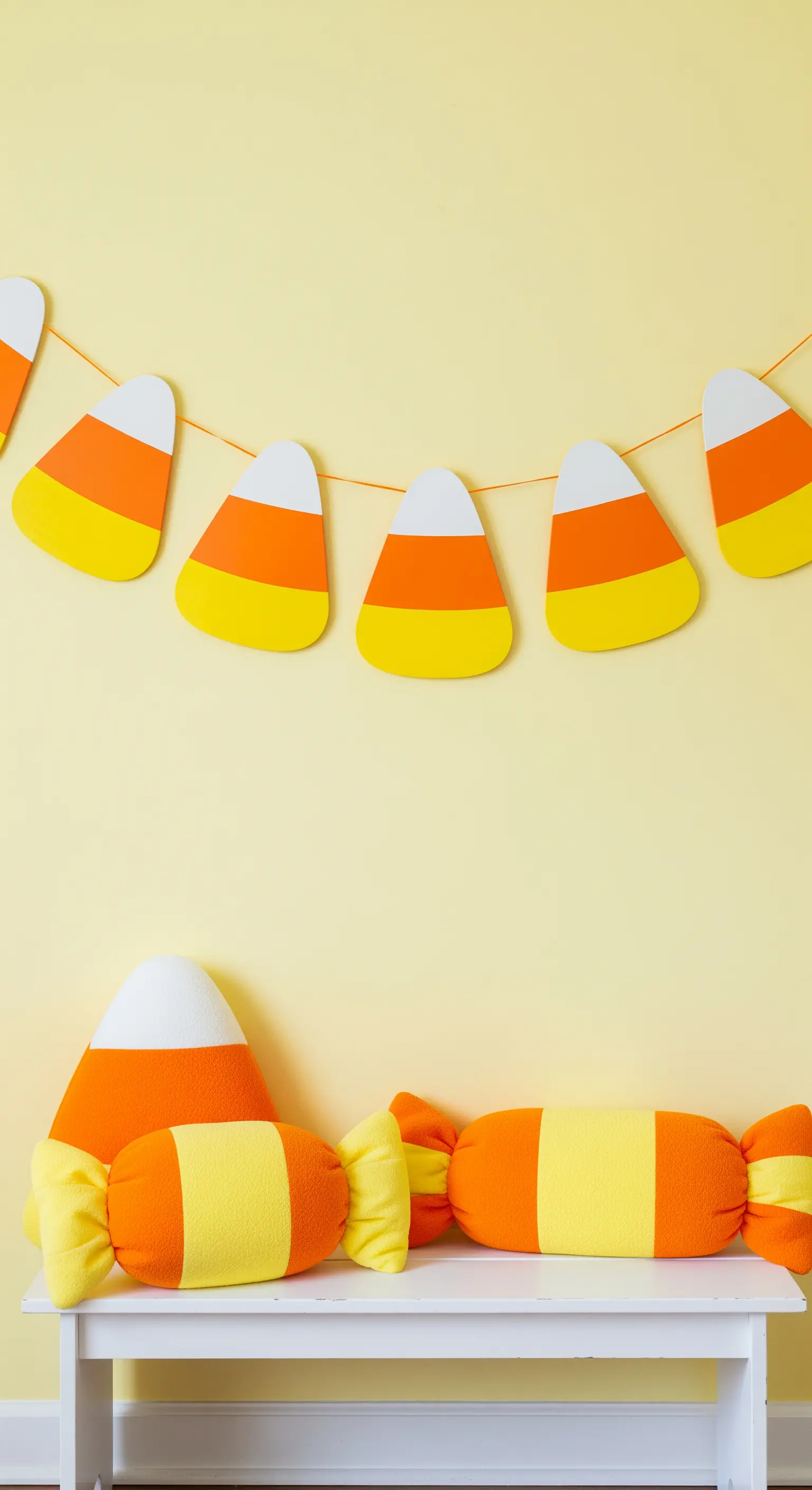 Eine Girlande aus Candy Corns an einer gelben Wand über passenden Kissen.