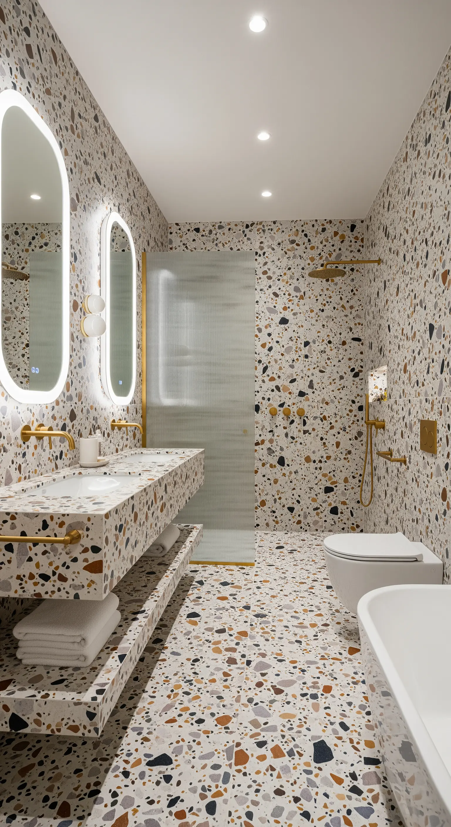 Modernes Badezimmer, vollständig mit hellem Terrazzo ausgekleidet, mit goldenen Armaturen.
