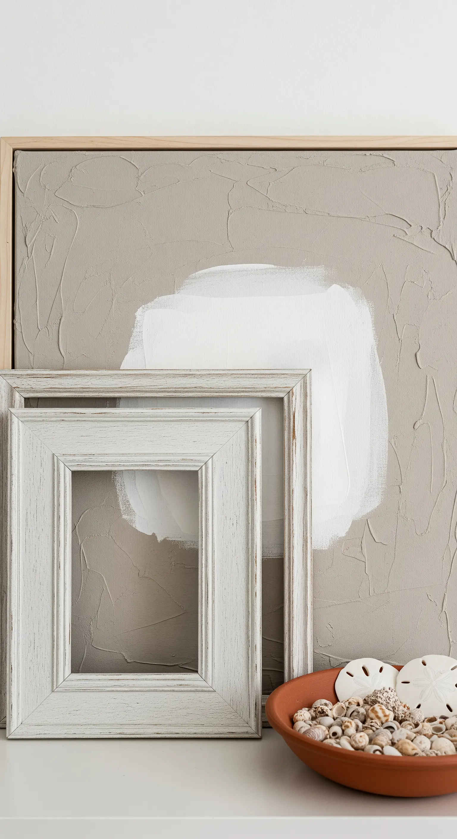 Gedeckte Deko mit strukturiertem Bild, leeren Bilderrahmen und Muscheln.