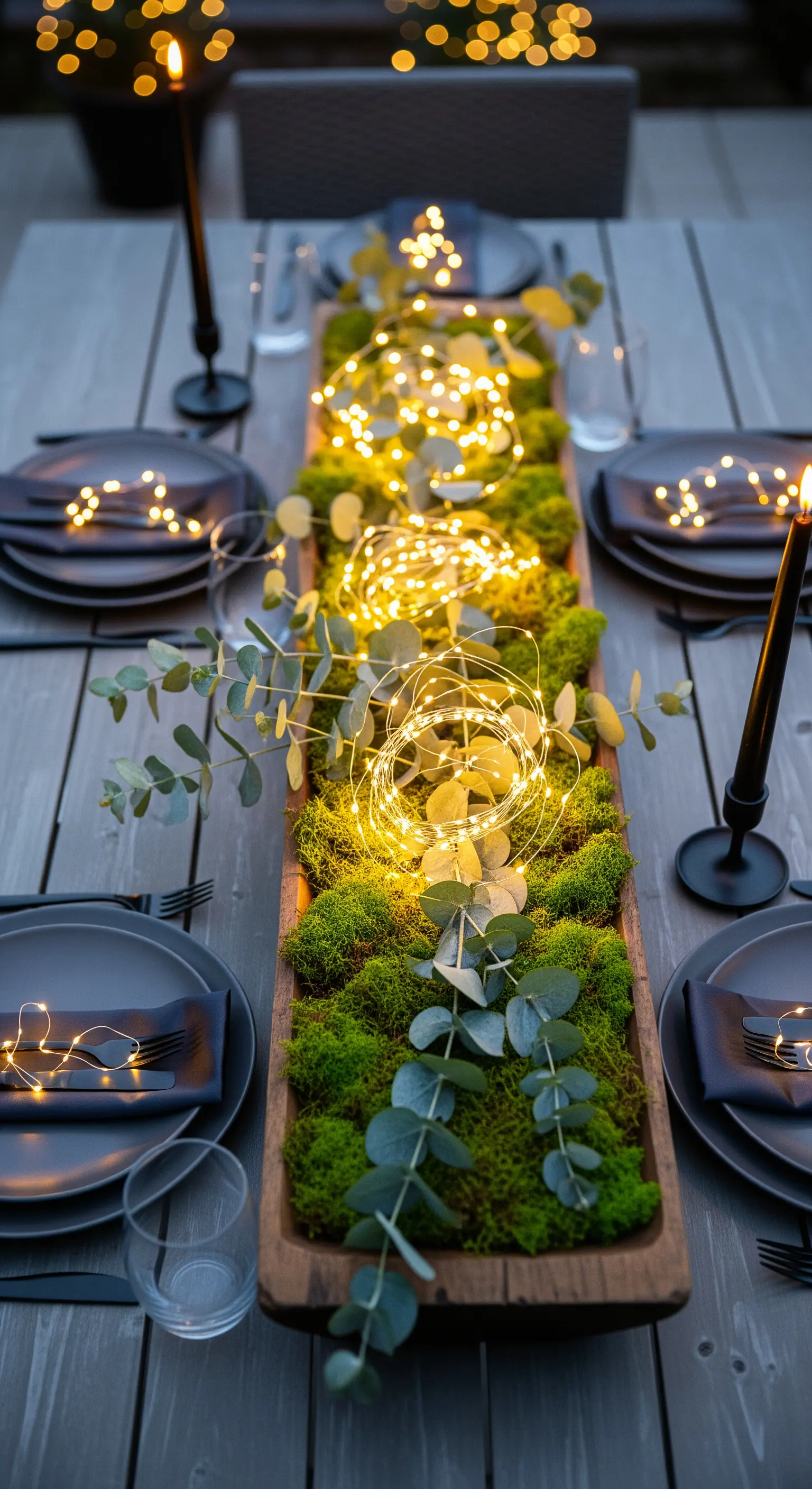 Holztrog mit Moos, Eukalyptus und Lichterketten als elegante Outdoor-Tischdeko.