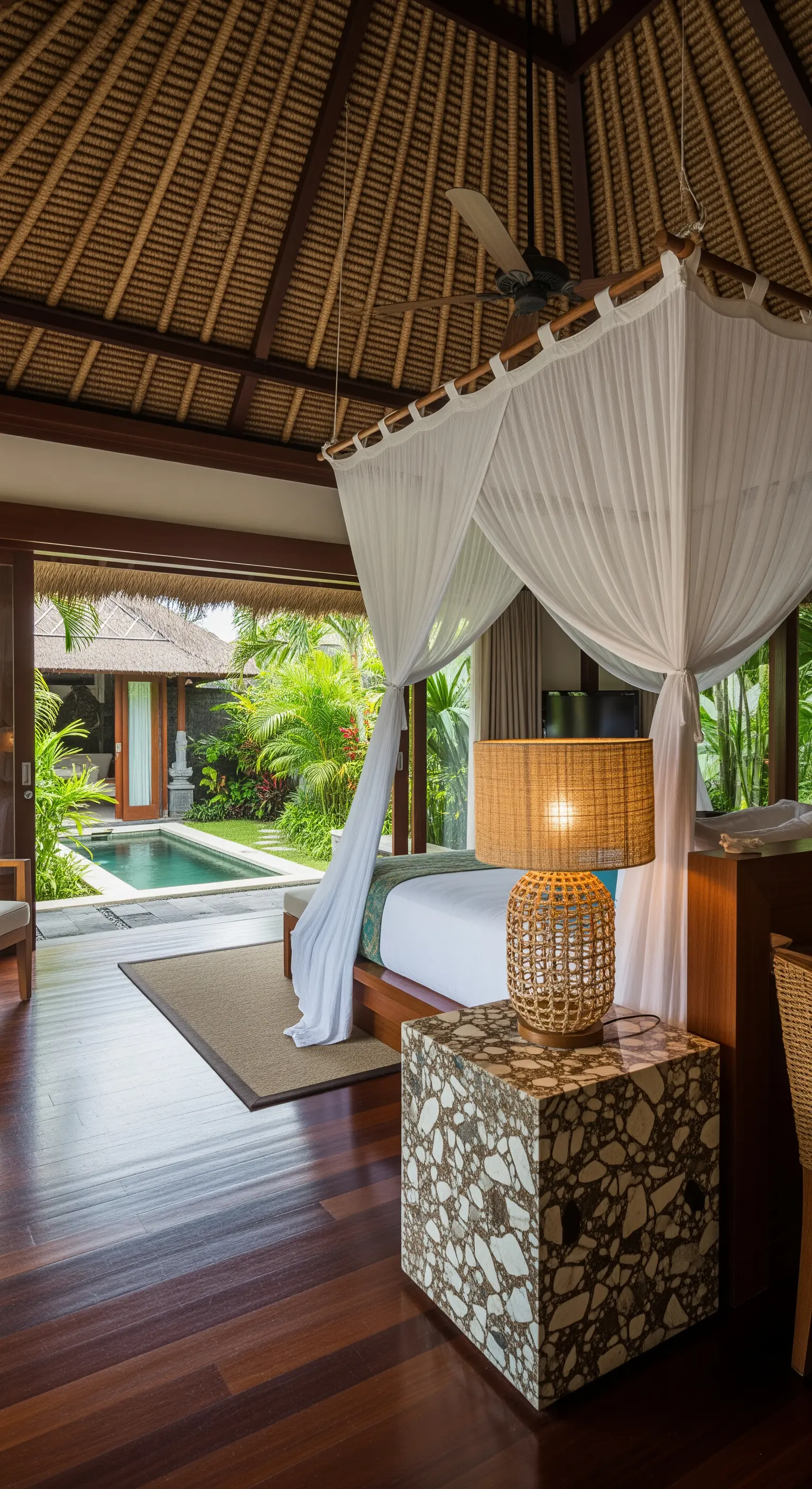 Tropisches Schlafzimmer mit Blick auf den Pool, Terrazzo-Nachttisch und Rattan-Lampe.