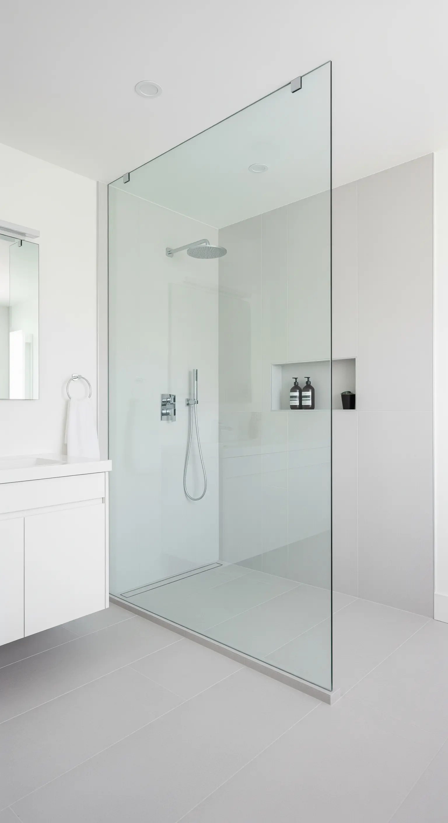 Bodengleiche Dusche mit einer einzigen, rahmenlosen Glaswand in einem weißen Badezimmer.