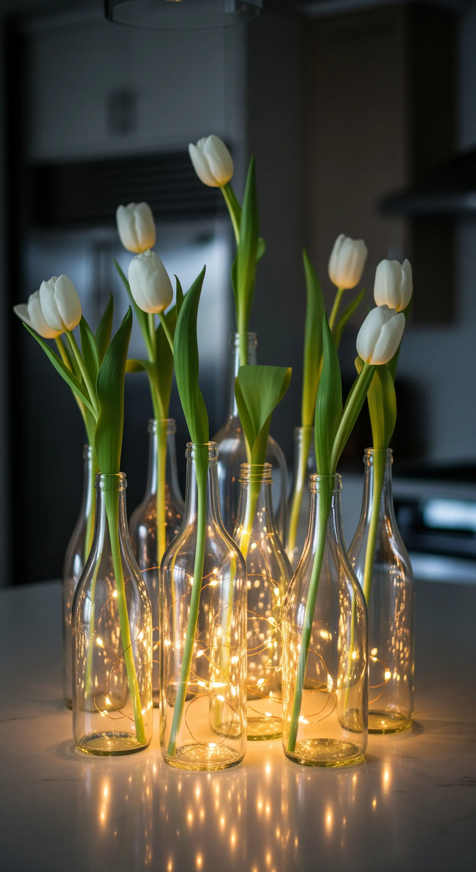 Mehrere Glasflaschen mit Lichterketten im Inneren, die als Vasen für weiße Tulpen dienen.