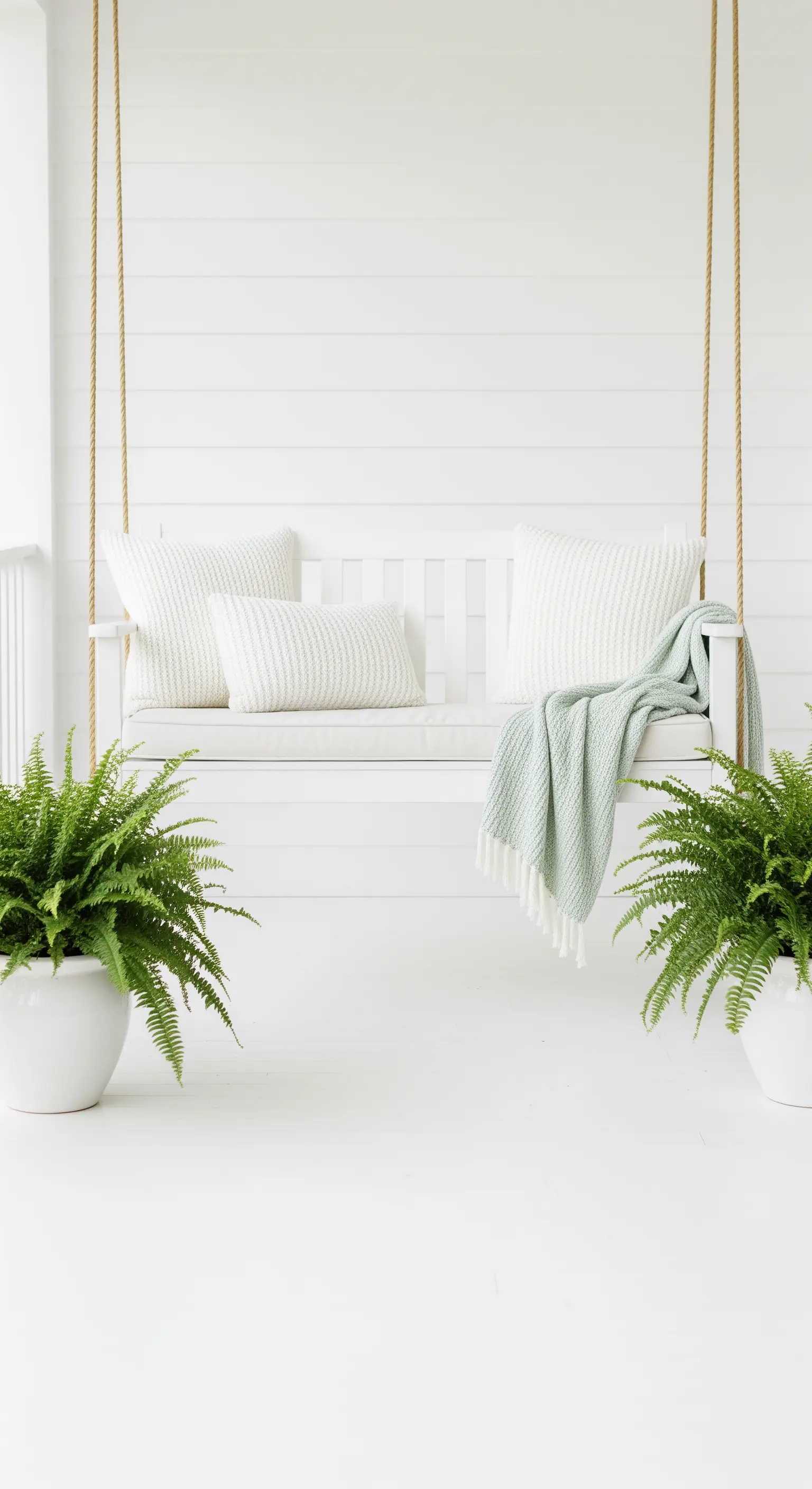 Weiße Veranda-Schaukel mit mintgrünem Plaid und Farnen